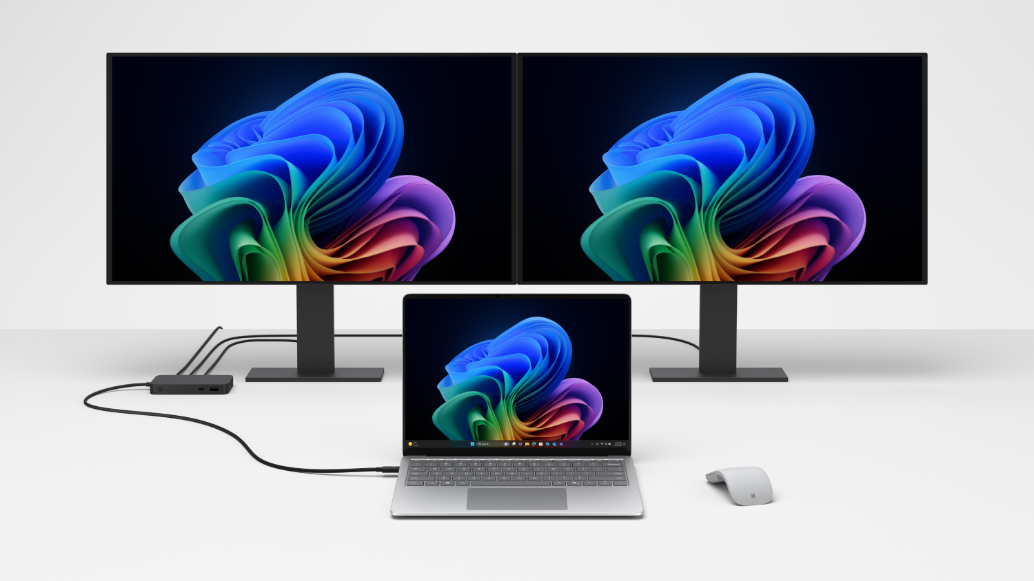 Dos monitores con una pantalla colorida, un portátil y un ratón sobre una superficie blanca. Los cables conectan los dispositivos.