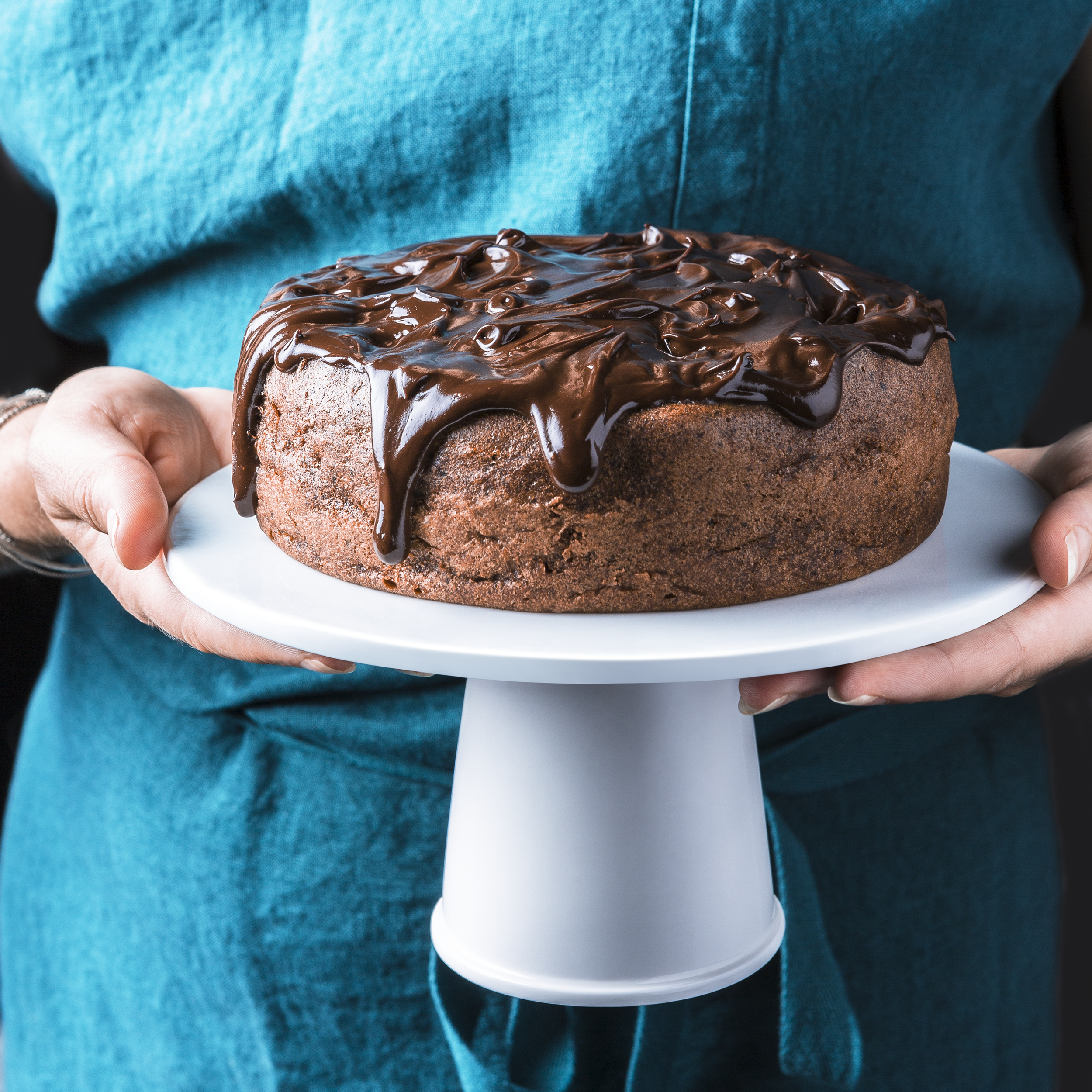 Személy csokoládétortát tart fehér tortaállványon.