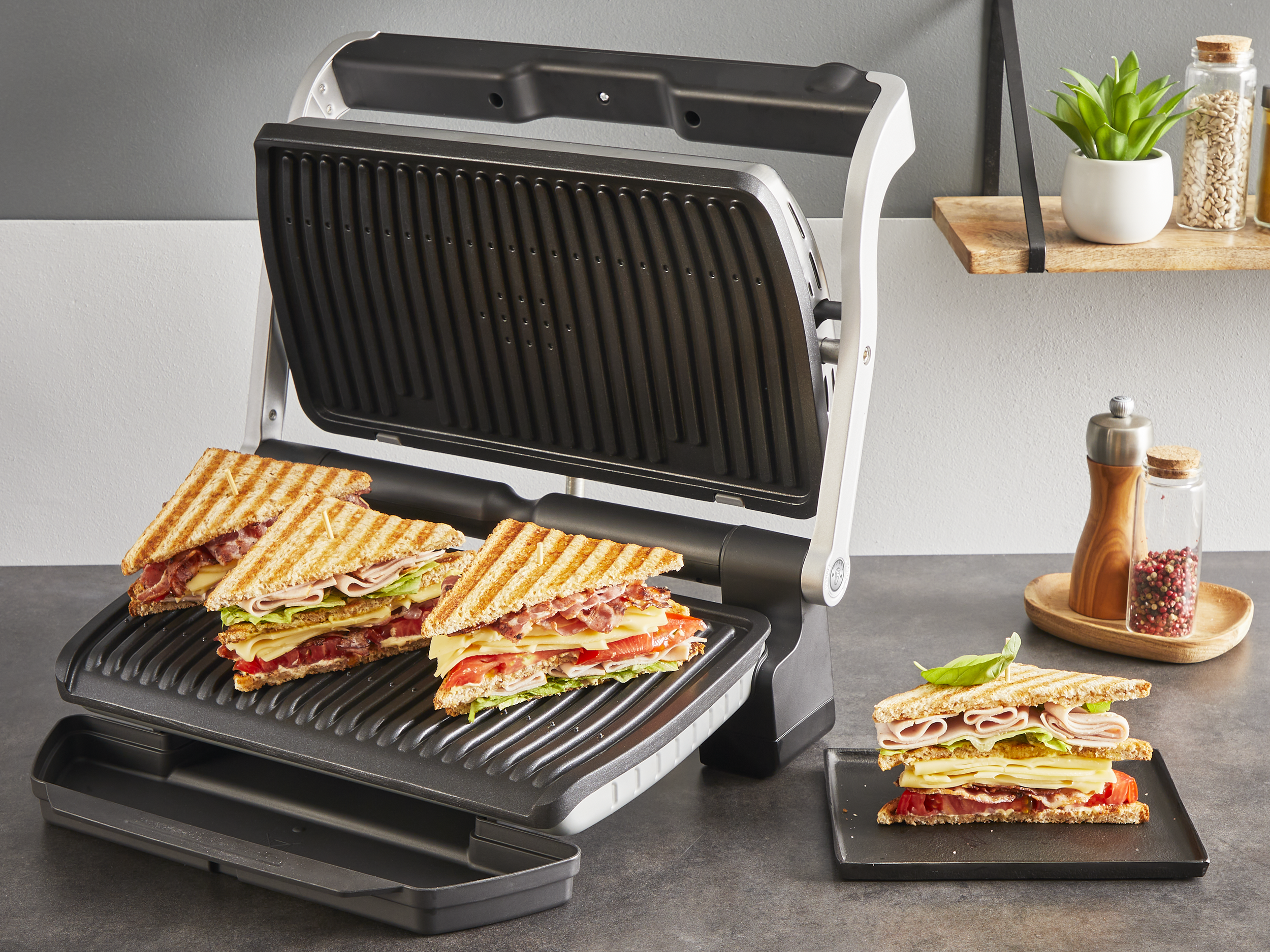 Grill szendvicsekkel, kettő a grillen, egy tányéron, hozzávalókkal.