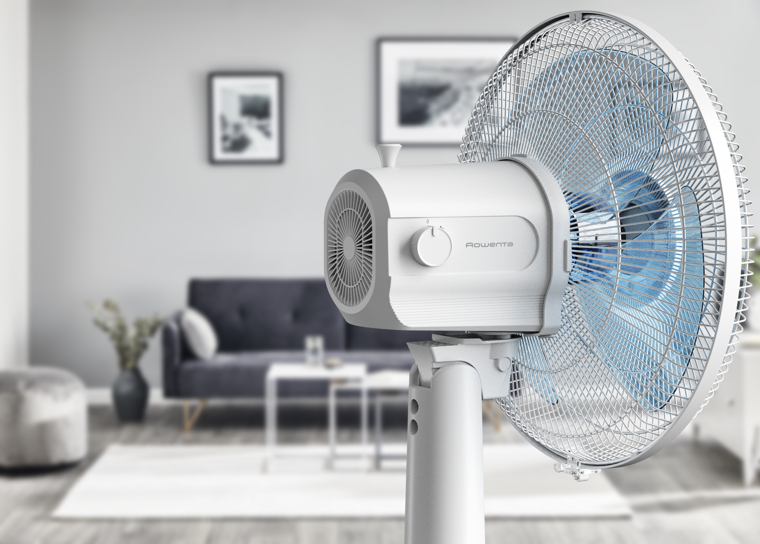 Fehér ventilátor kék lapátokkal egy állványon, homályos nappali háttérrel.