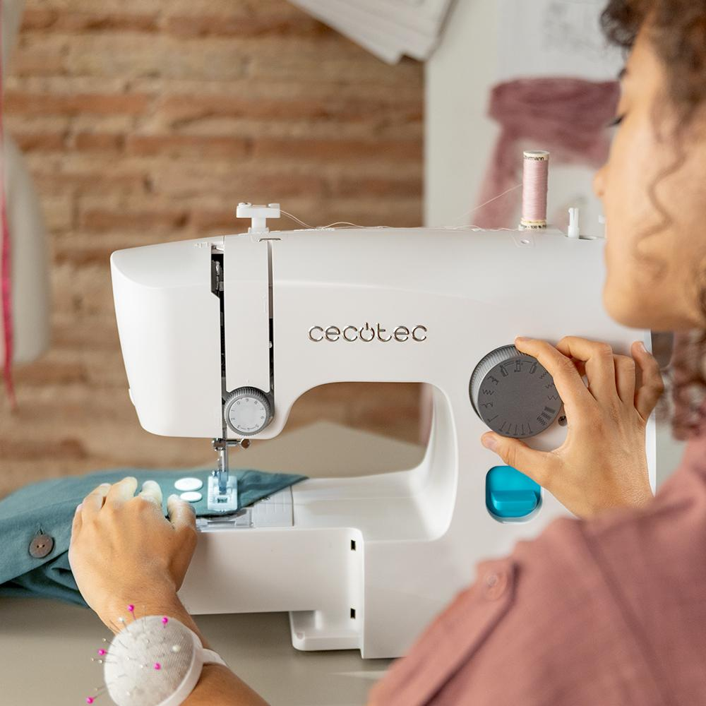 Una persona usando una máquina de coser blanca, manos en los controles, con tela y alfileres.