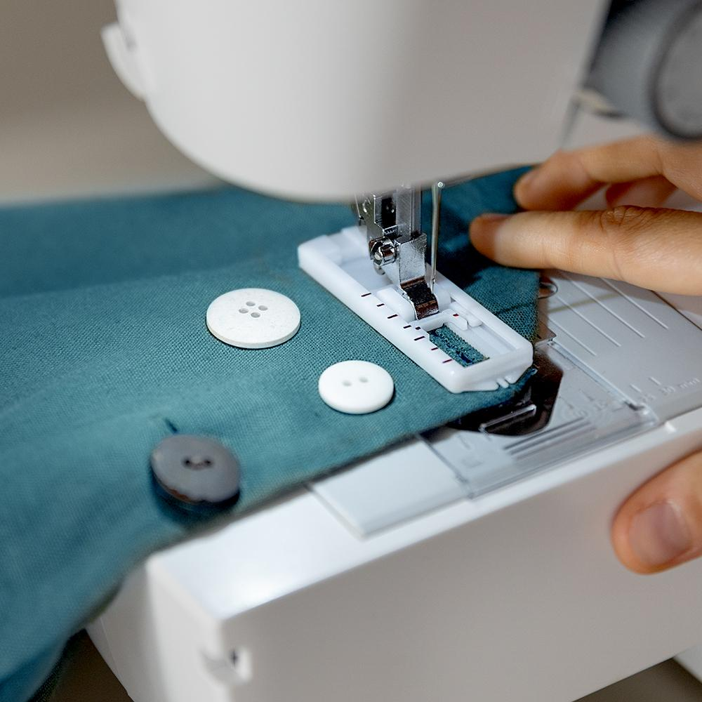 Una máquina de coser está cosiendo una ojal. Los botones están cerca.
