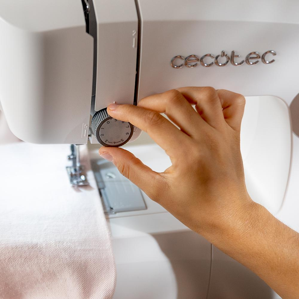 Una mano ajustando el dial en una máquina de coser blanca. La máquina es blanca con la marca visible.