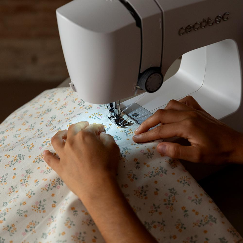 Manos cosiendo tela en una máquina de coser blanca, primer plano.