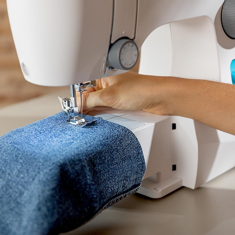 Una mano cosiendo tela vaquera con una máquina de coser blanca.