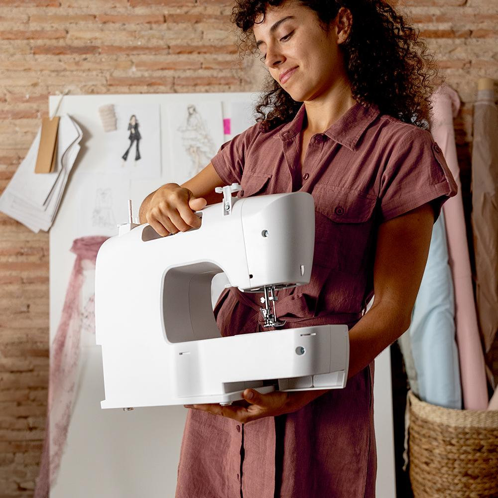 Una mujer sosteniendo una máquina de coser blanca, con un fondo de materiales de costura.