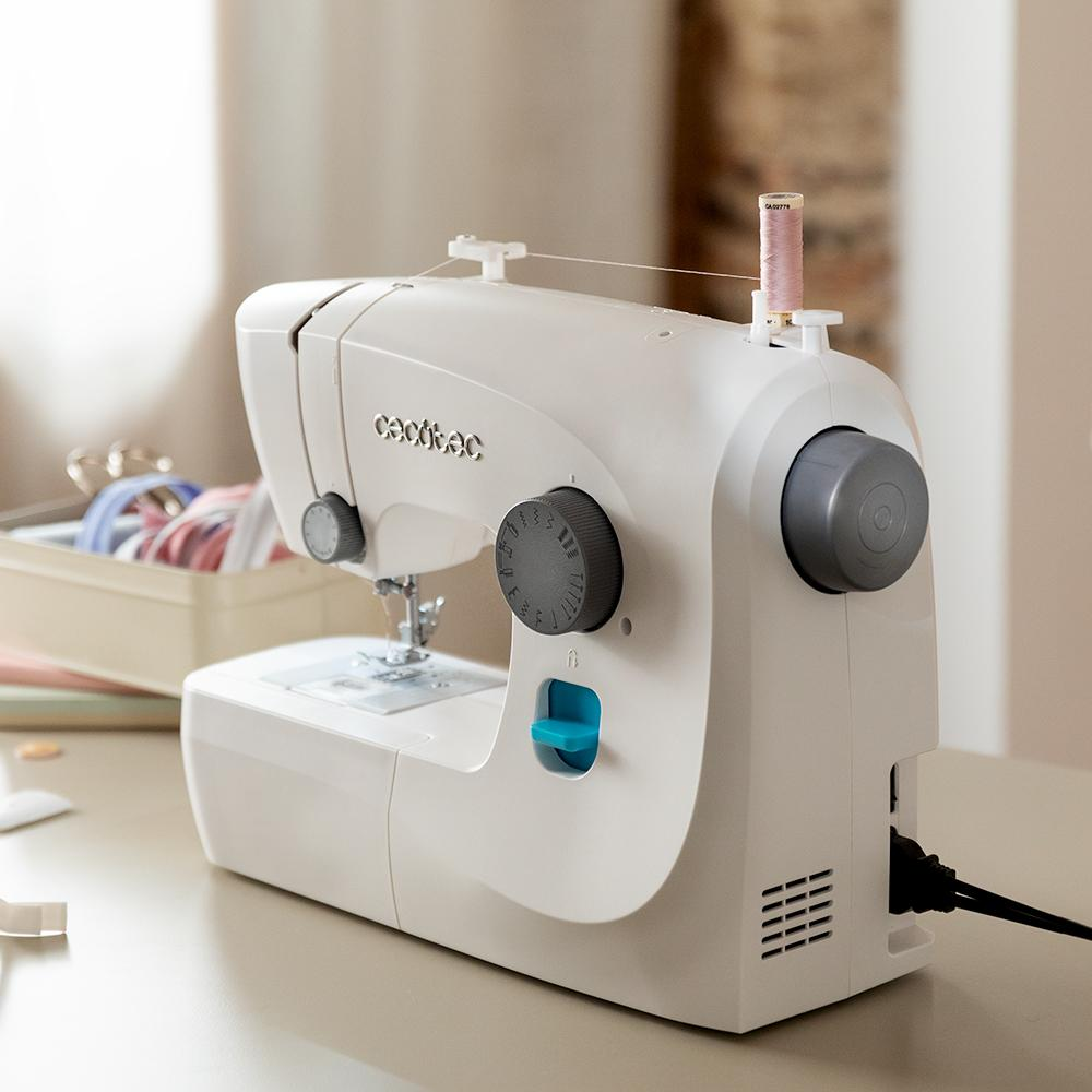 Una máquina de coser blanca sobre una mesa, con carretes de hilo y tijeras en el fondo.