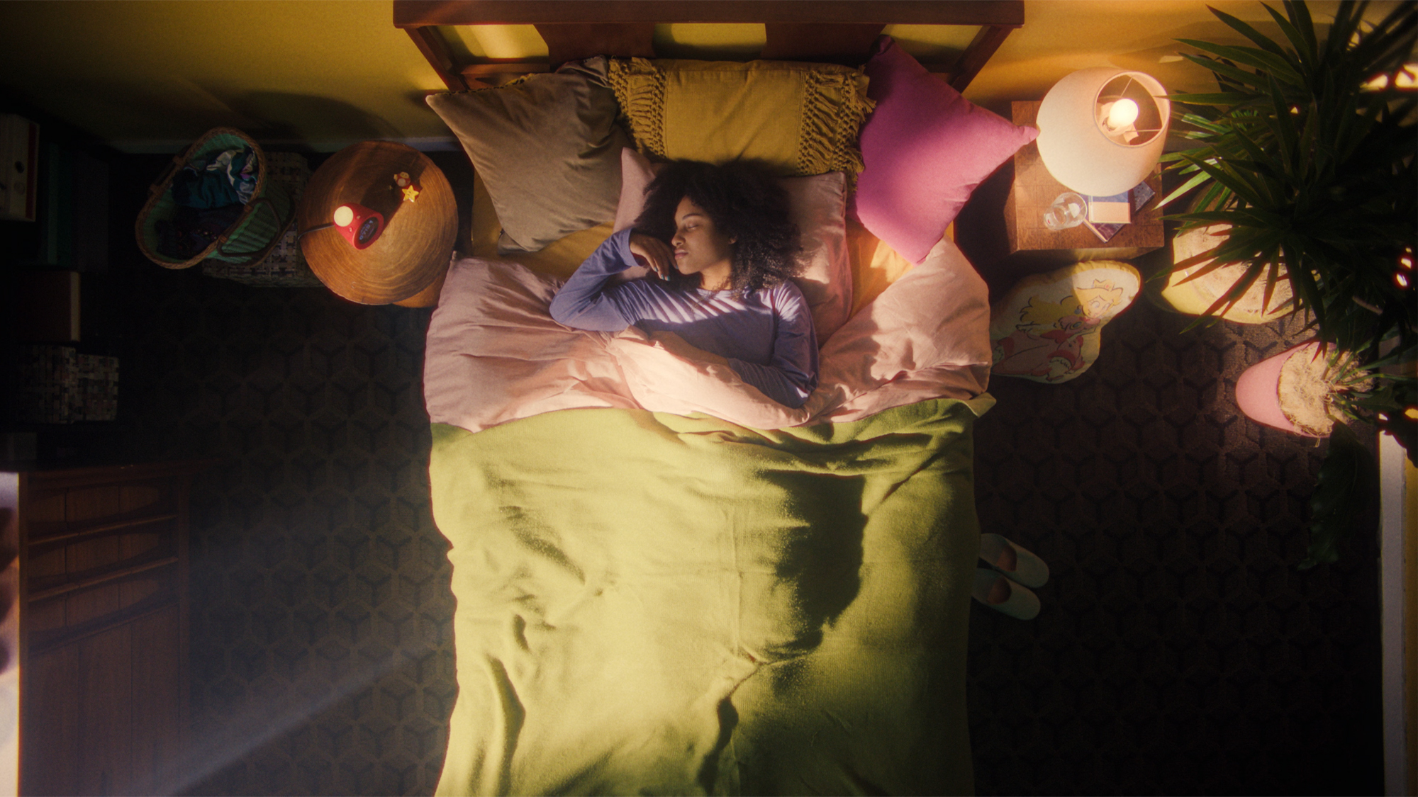 Vue aérienne d'une femme dormant dans son lit, entourée d'objets décoratifs dans une chambre.