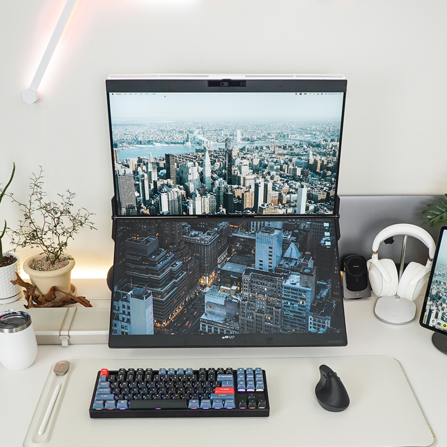 Dual-screen laptop on a desk with keyboard, mouse, and city skyline background on the screens.