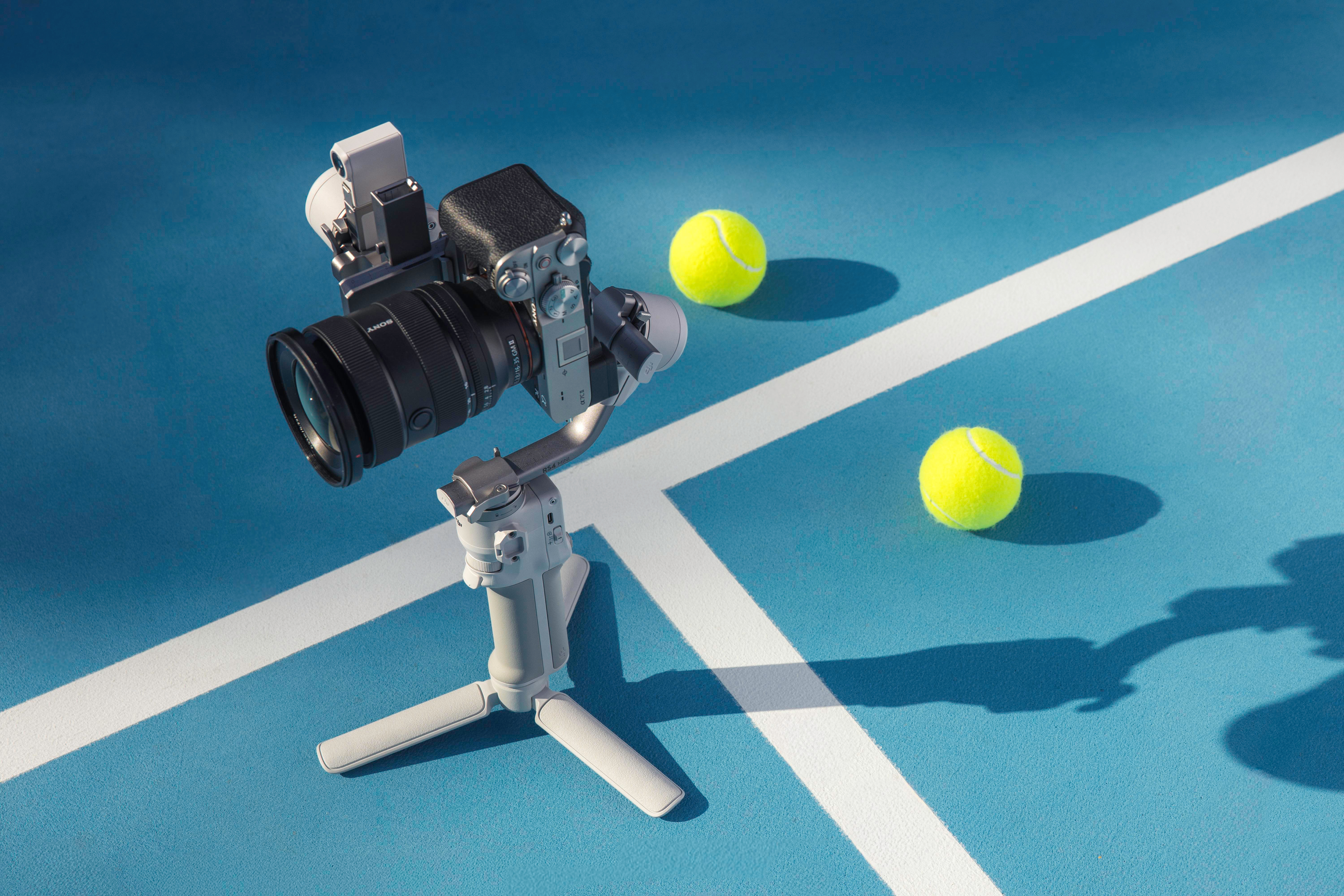 Kamera auf Stativ. Zwei Tennisbälle auf blauem Platz.