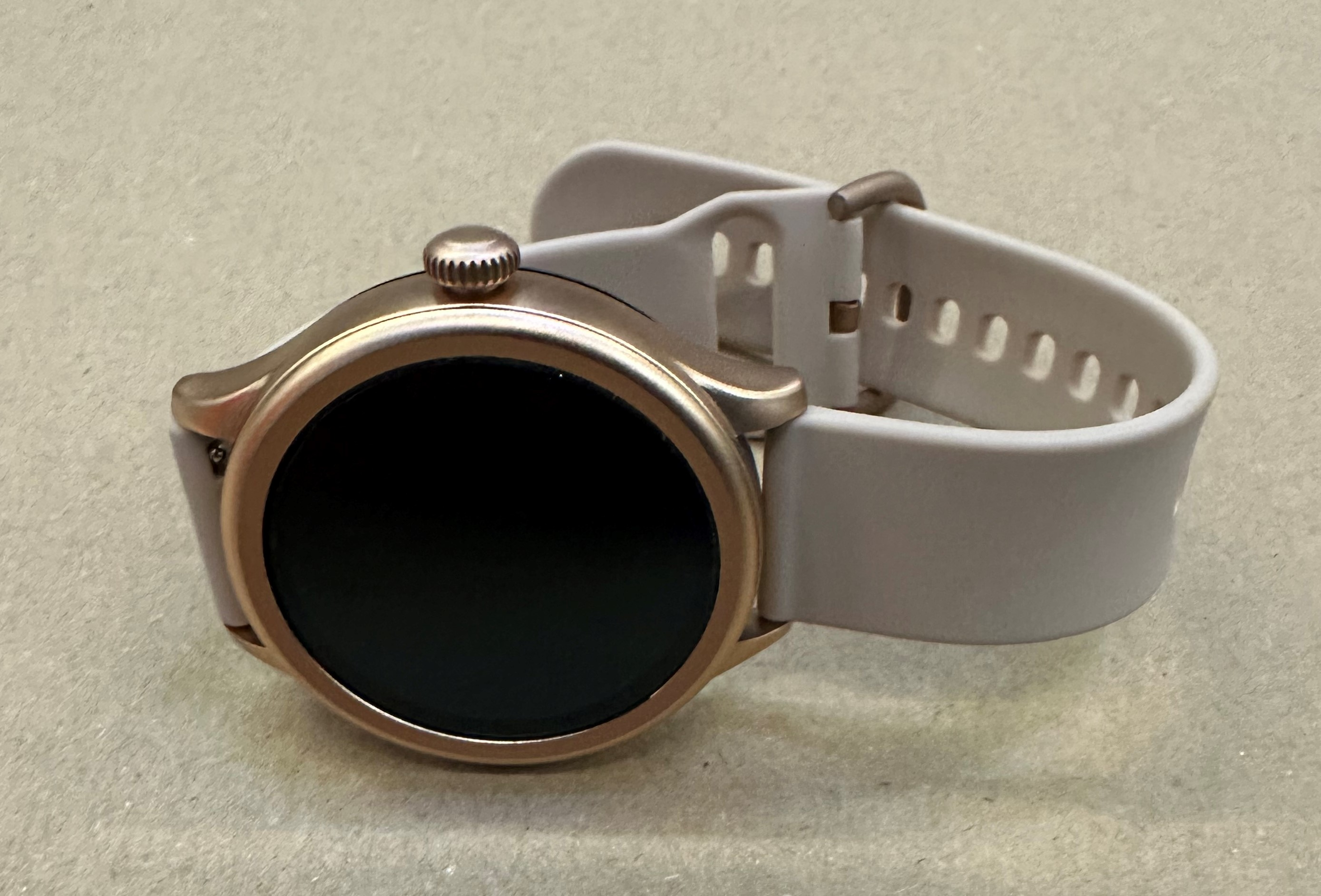 Złoty smartwatch z białym paskiem na teksturowanej powierzchni.