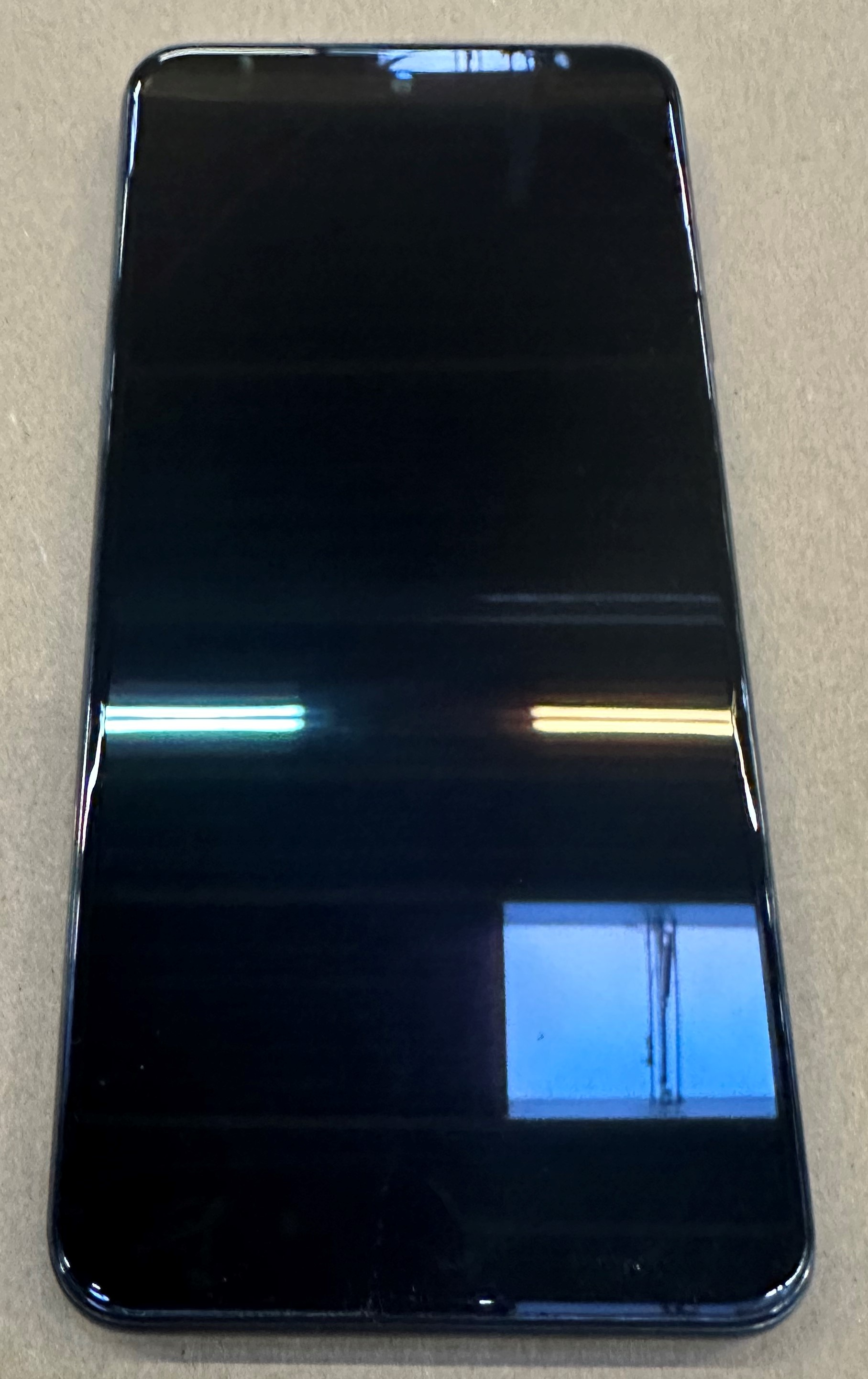 Czarny smartfon leży na szarej powierzchni. Widoczne są odbicia światła.