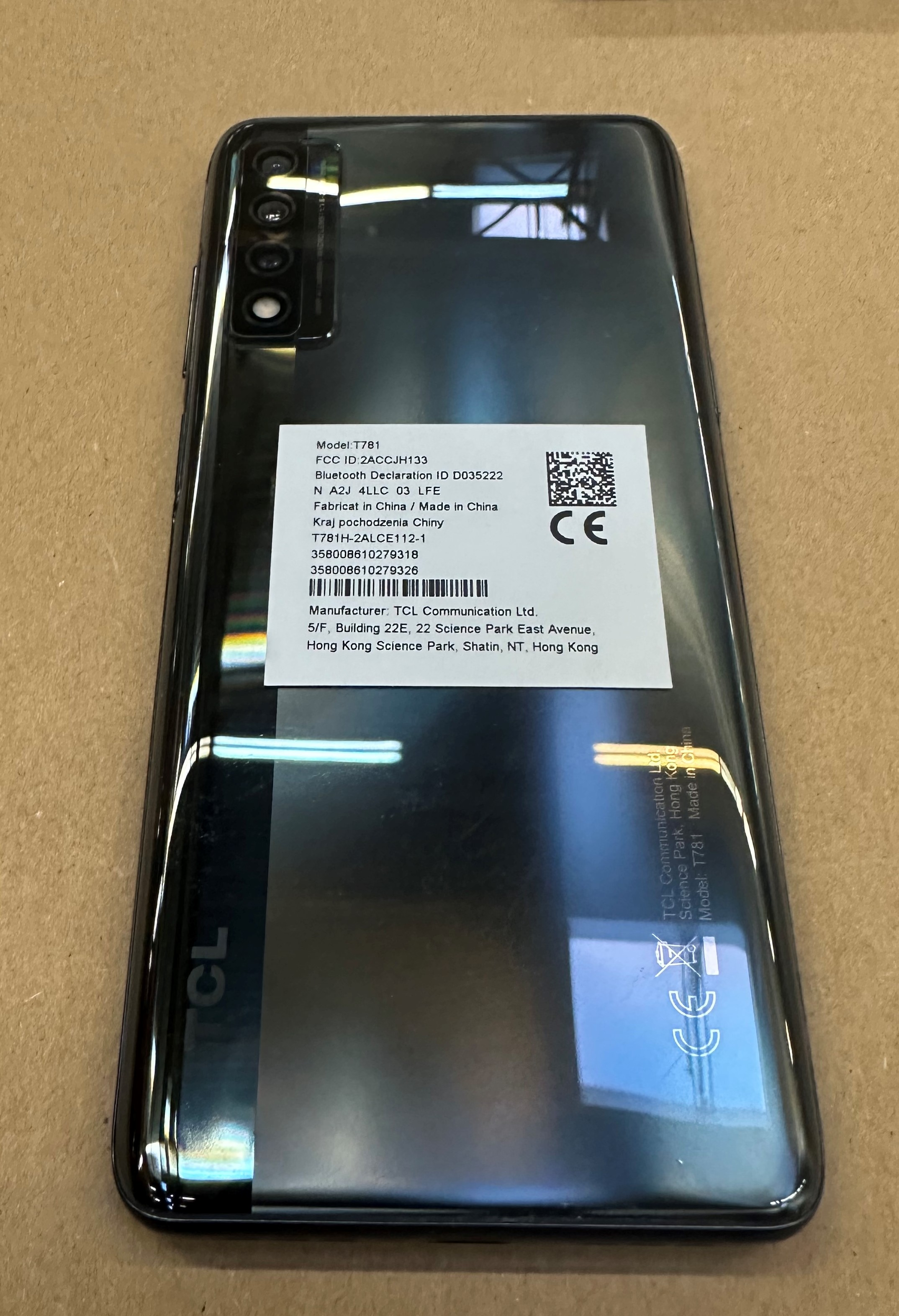 Tył czarnego smartfona TCL T781 z czterema aparatami i etykietami.