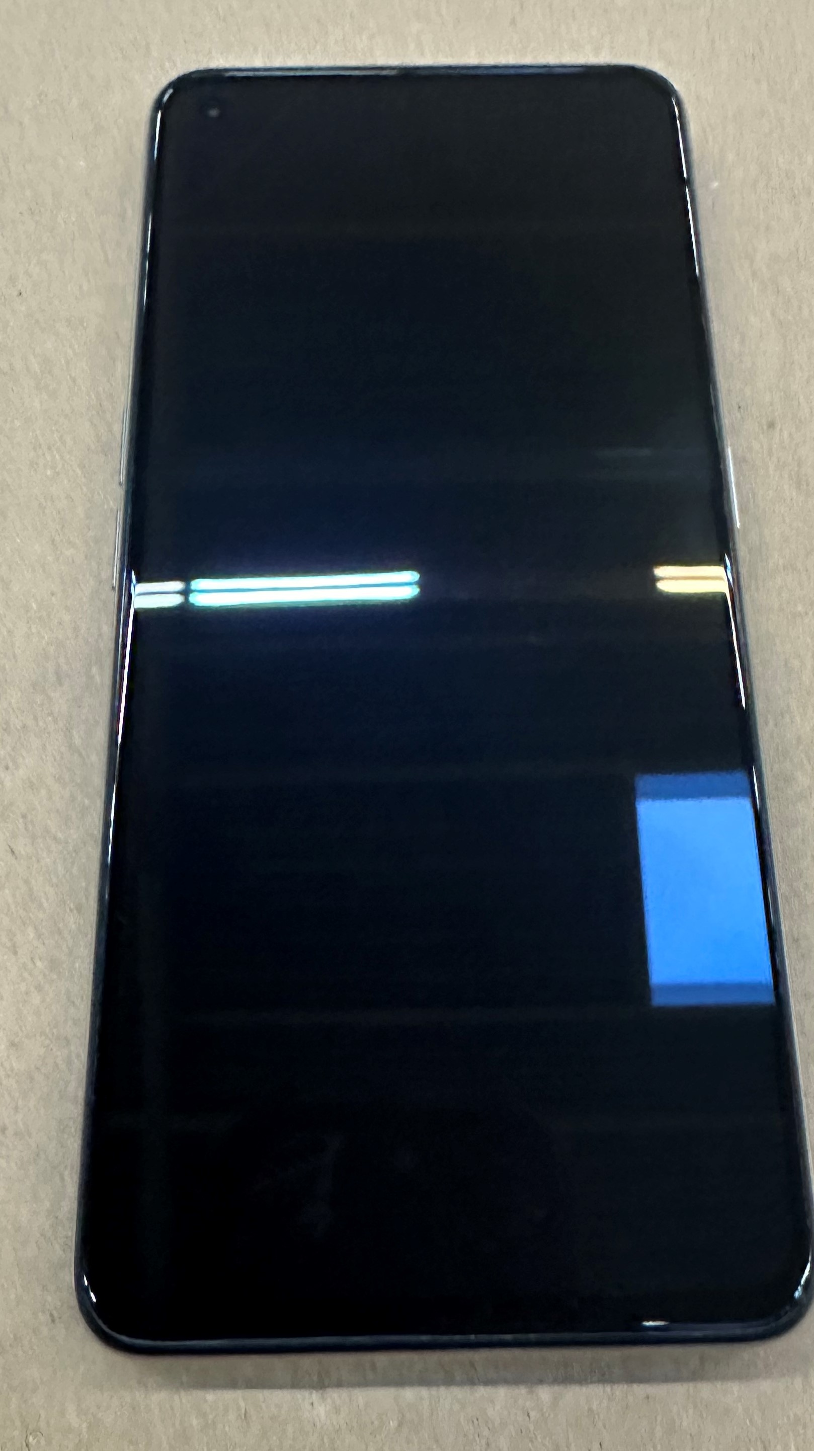 Ciemny smartfon z niebieskim prostokątem na ciemnym ekranie.