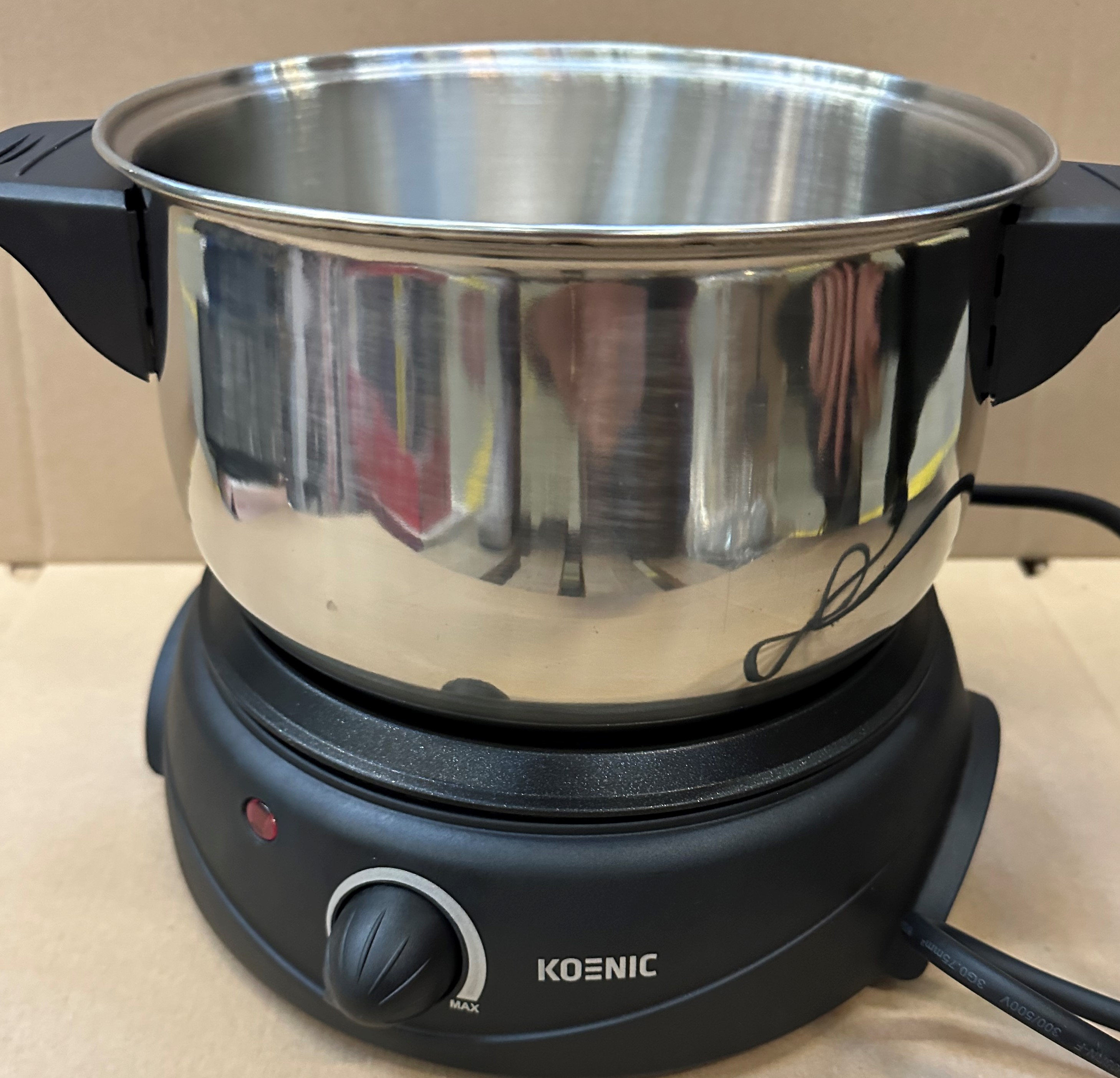 Garnek do fondue ze stali nierdzewnej na czarnej podstawie elektrycznej z pokrętłem. Białe tło.