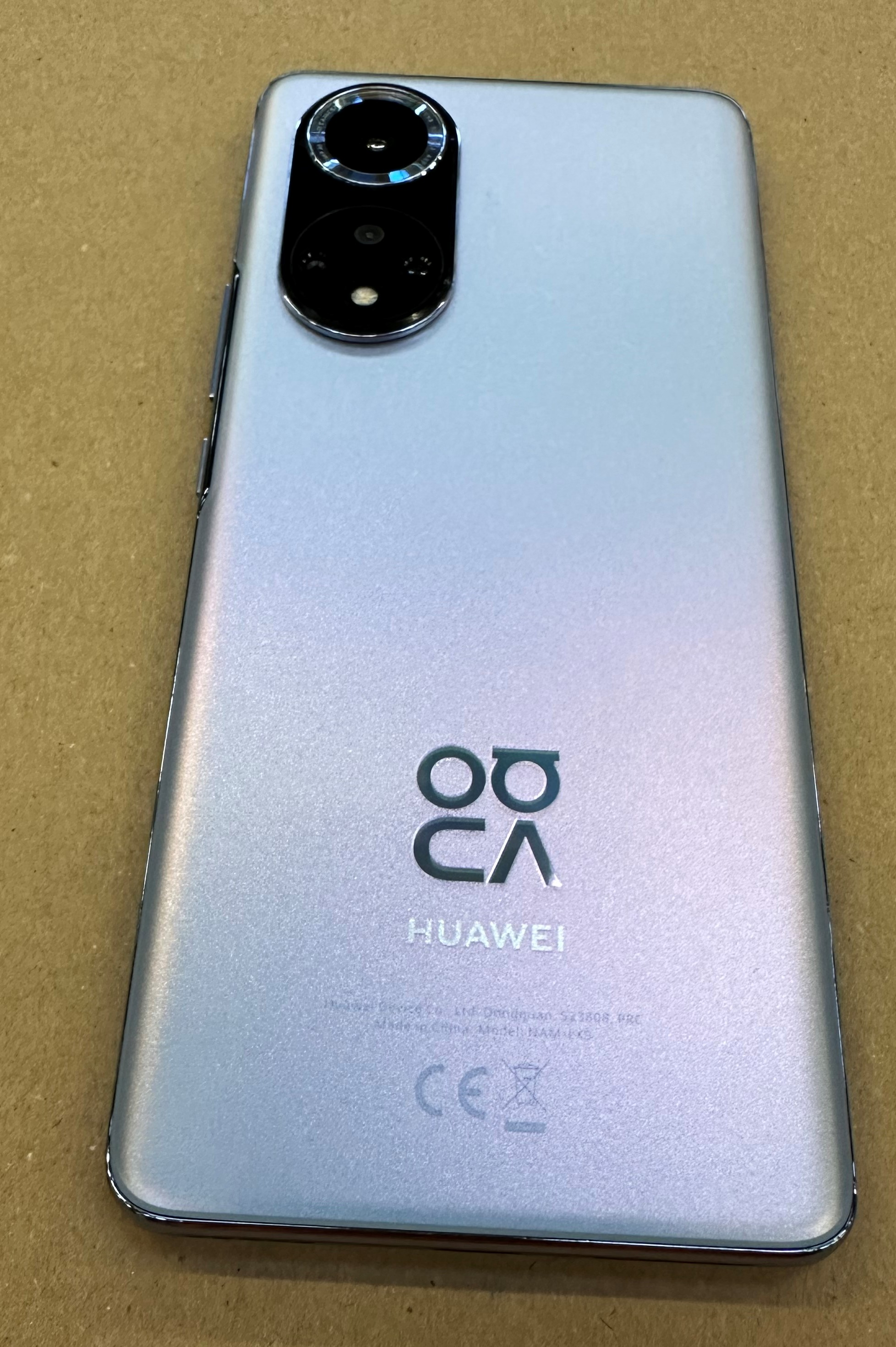 Srebrny telefon Huawei z dwoma aparatami i logo Huawei z tyłu, na brązowej powierzchni.