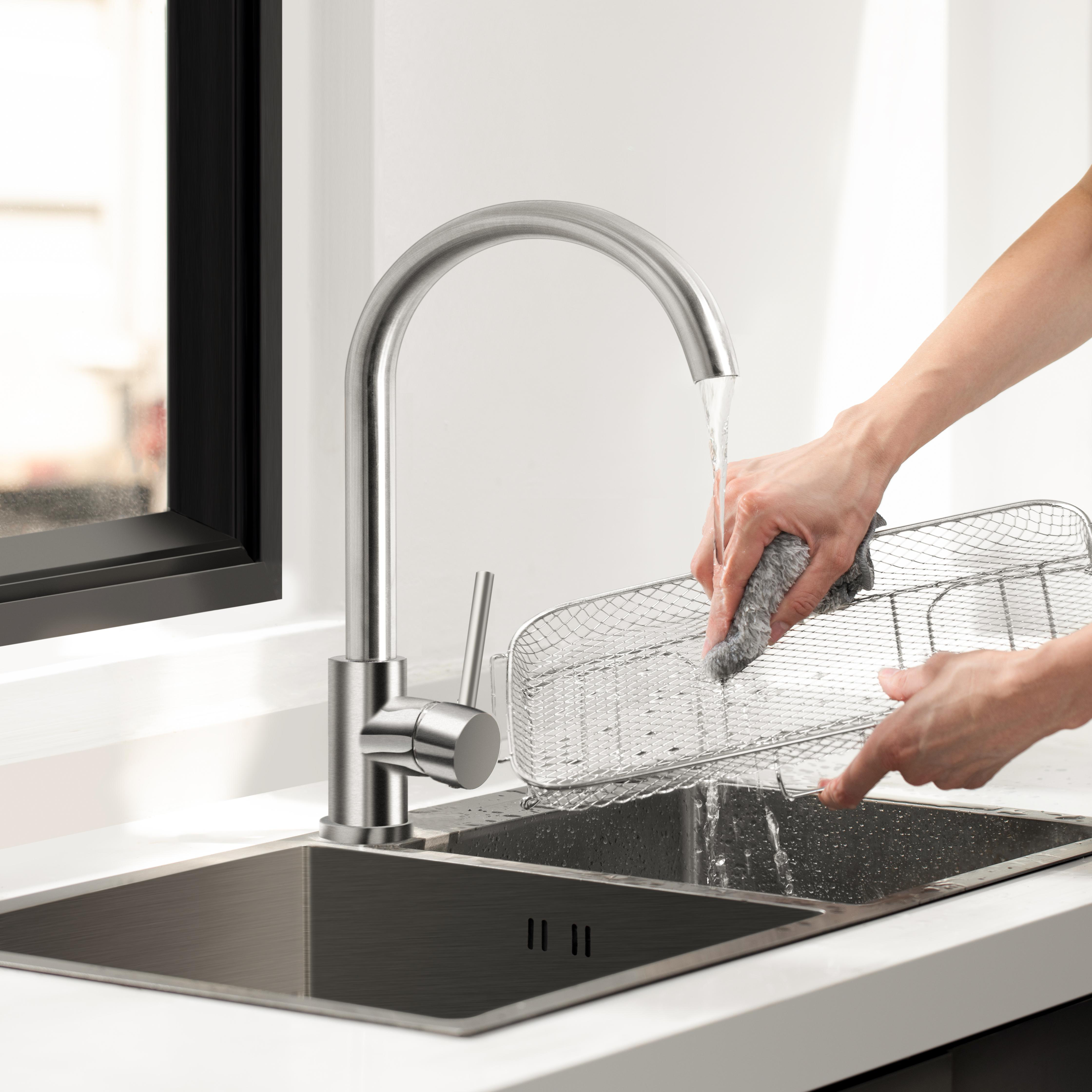 Eine Person wäscht ein Metallsieb unter einem Küchenwasserhahn.