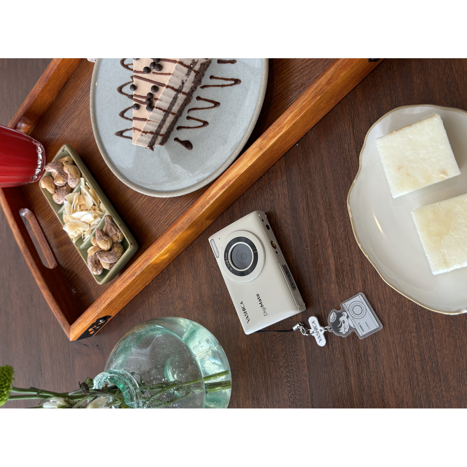 Een camera, cake, noten en een drankje op een houten dienblad op een tafel.