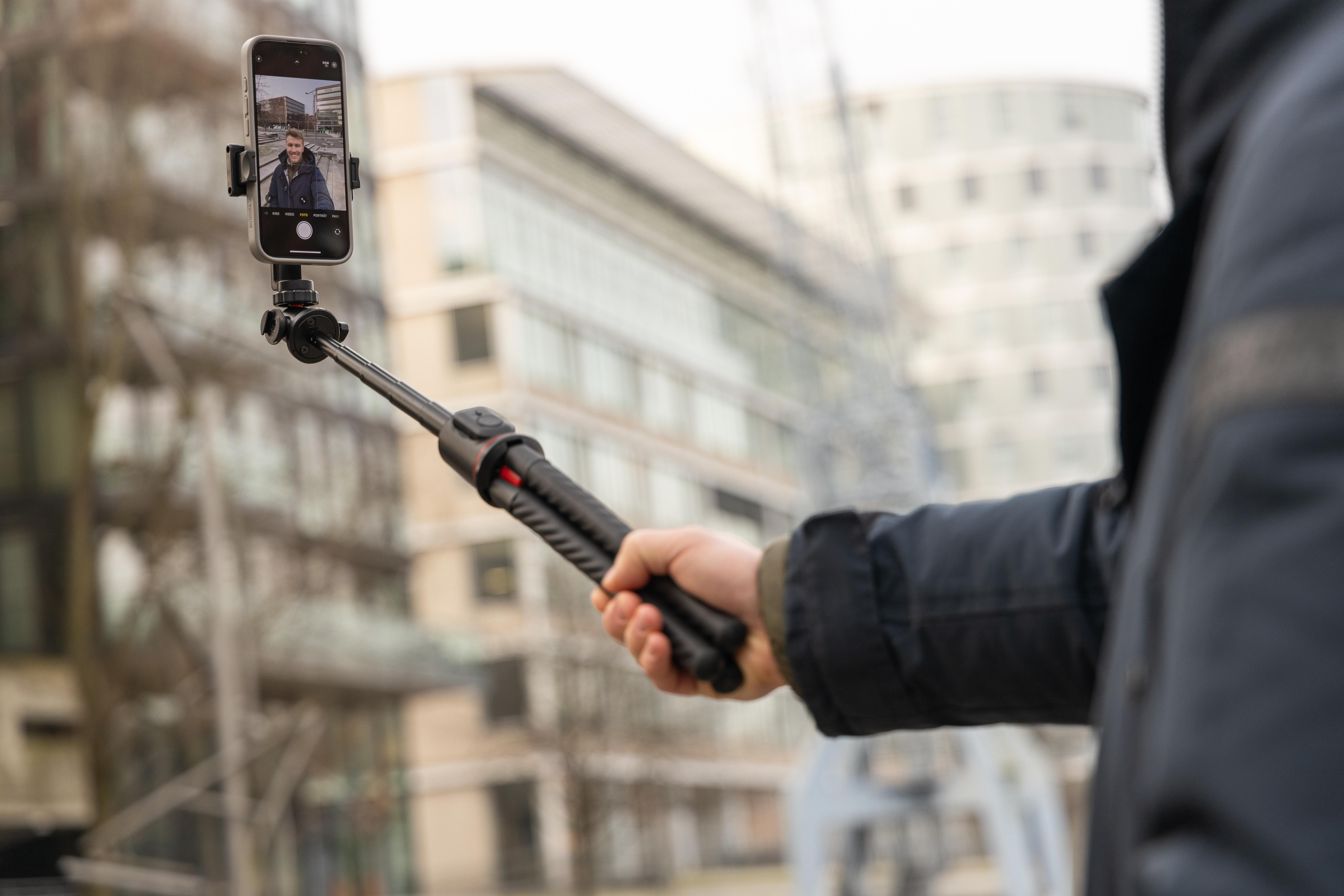 Person hält Selfie-Stick mit Telefon, das das Bild einer Person zeigt.
