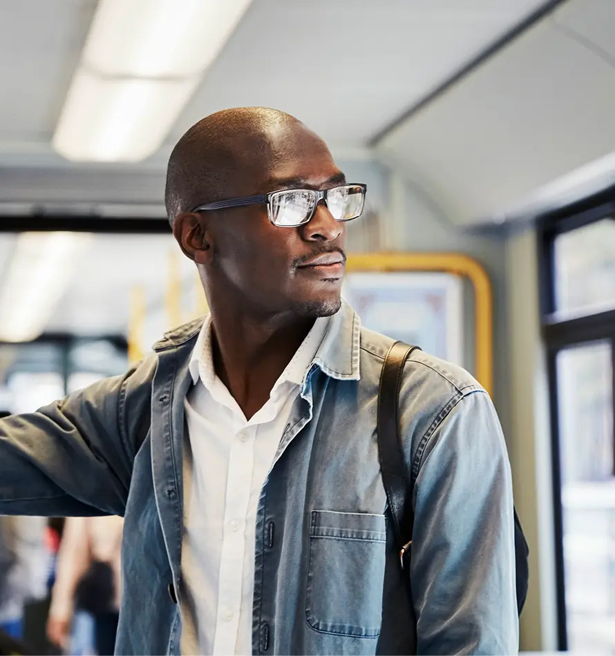 Homme avec des lunettes dans un train, regardant par la fenêtre ; portant une veste en jean et une chemise blanche.