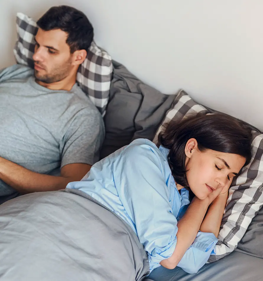 Un couple au lit, l'homme regarde ailleurs, la femme dort sur le côté.