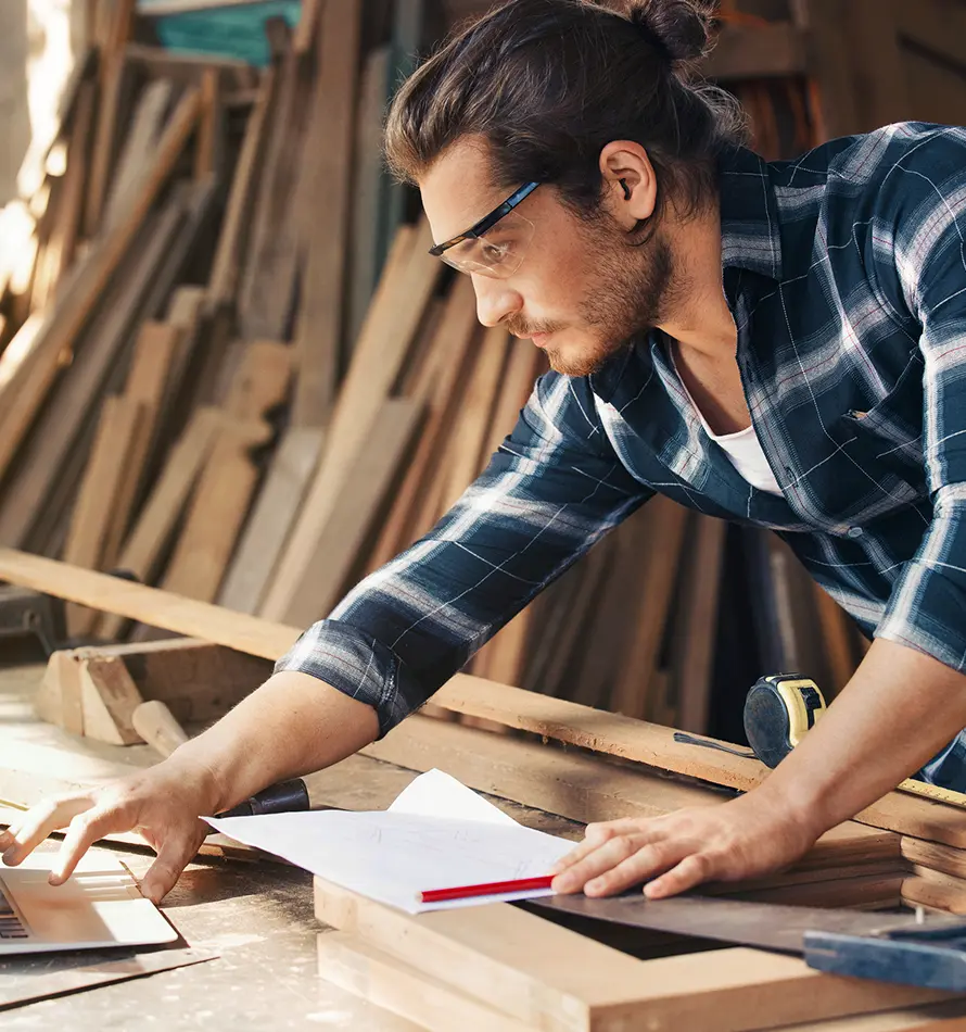 Un homme portant des lunettes travaille dans un atelier, regardant un laptop.
