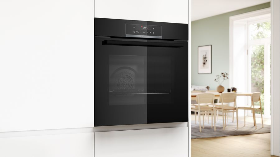 Horno cerrado con frontal negro y puerta de cristal. El fondo muestra armarios blancos y una cocina.