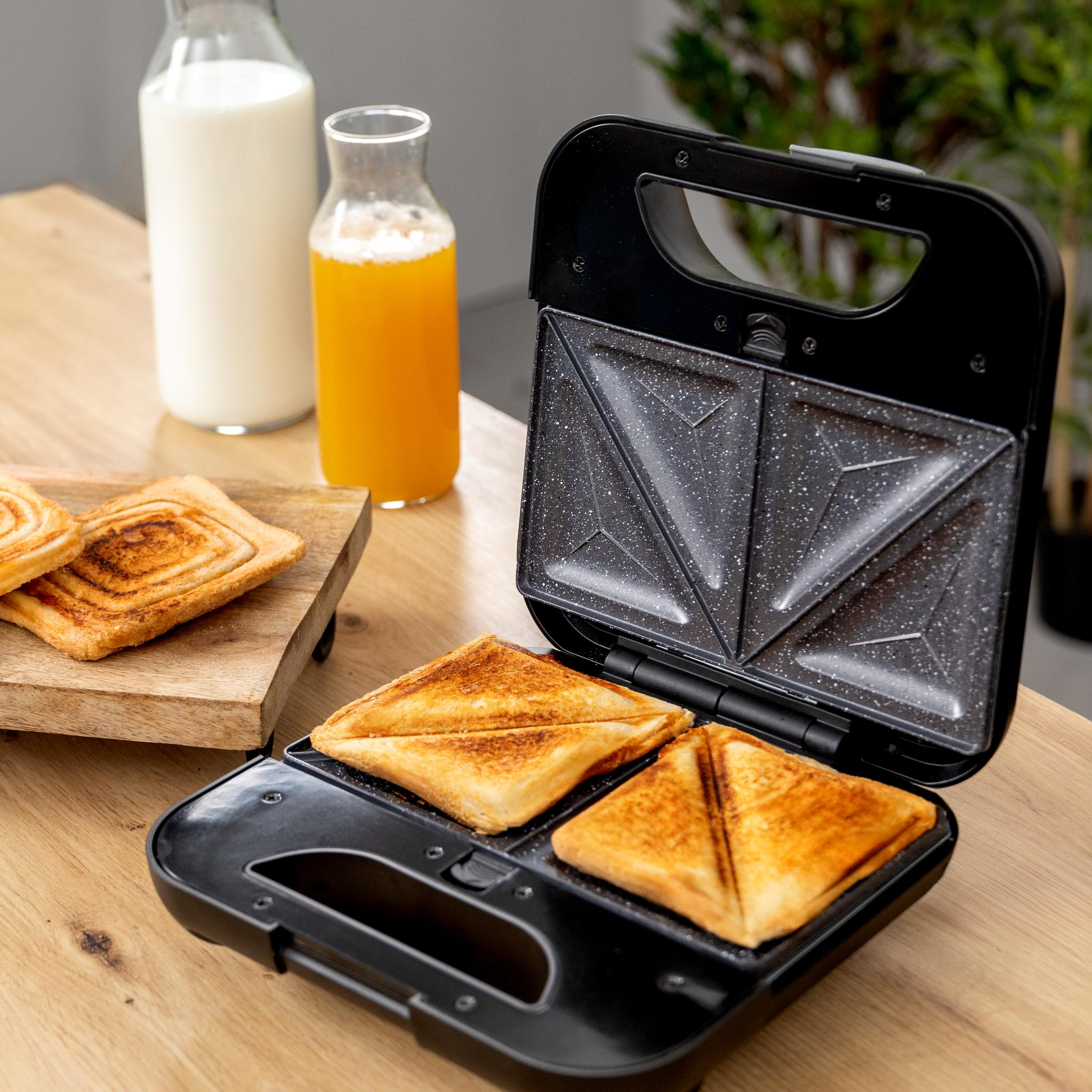 Sandwichera con dos sándwiches, leche y zumo de naranja.