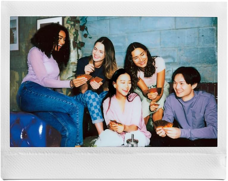 Öt ember ül, mosolyog, kártyázik. Fehér polaroid képkeret veszi körül a képet.