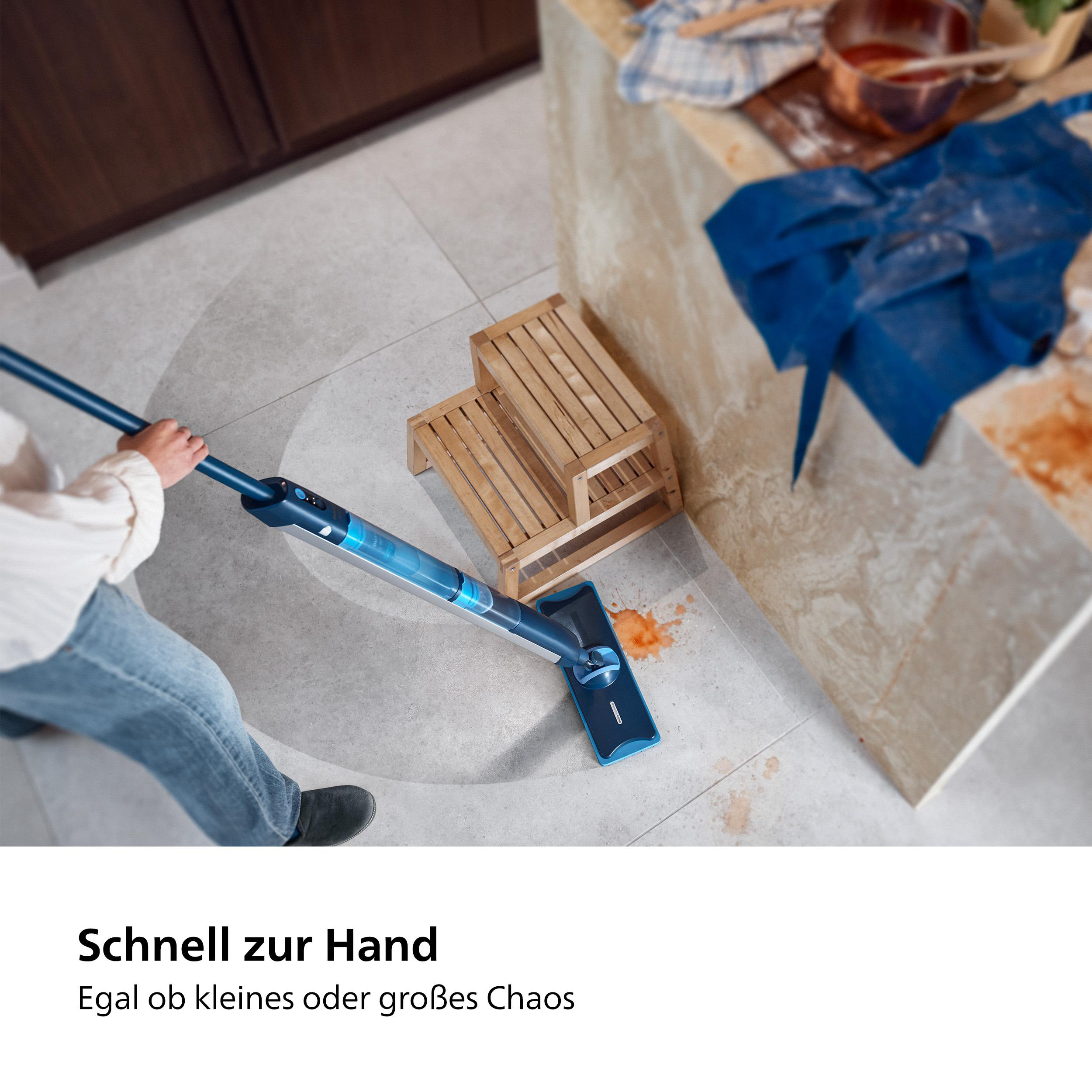 Person, die einen blauen Wischmopp auf einem Fliesenboden mit verschütteten Lebensmitteln benutzt.