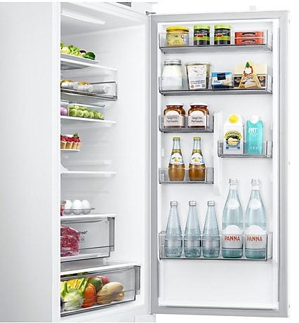 Otwarta biała lodówka wypełniona produktami spożywczymi w szufladach i na półkach.