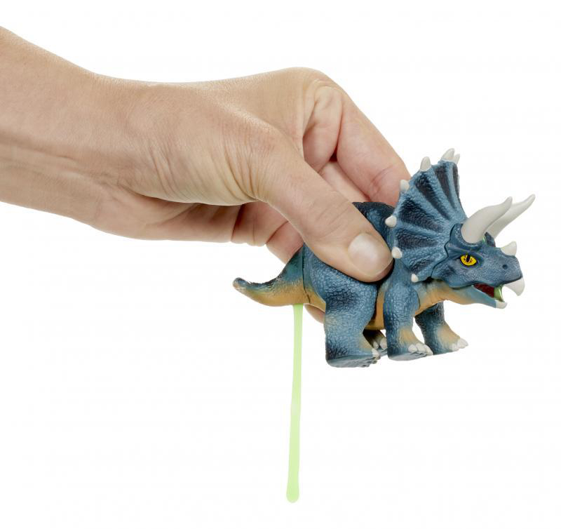 Hand, die ein Spielzeug-Dinosaurier quetscht. Grüner Schleim kommt aus dem Hintern des Dinosauriers.