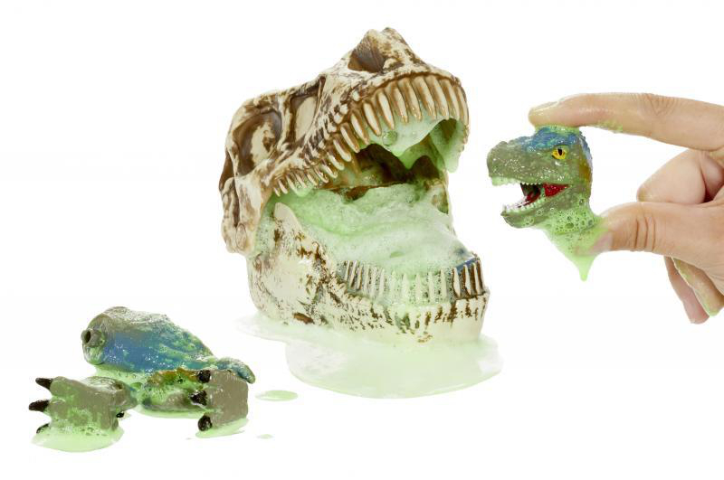 Dinosaurierschädel mit grünem Schleim. Eine Hand hält einen kleinen Dino-Kopf. Ein Dino-Fuß liegt am Boden.
