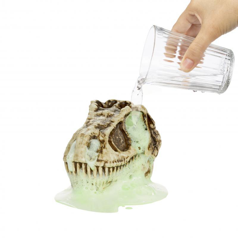 Eine Hand, die Wasser in einen Dinosaurierschädel gießt, wobei grüner Schaum freigesetzt wird.