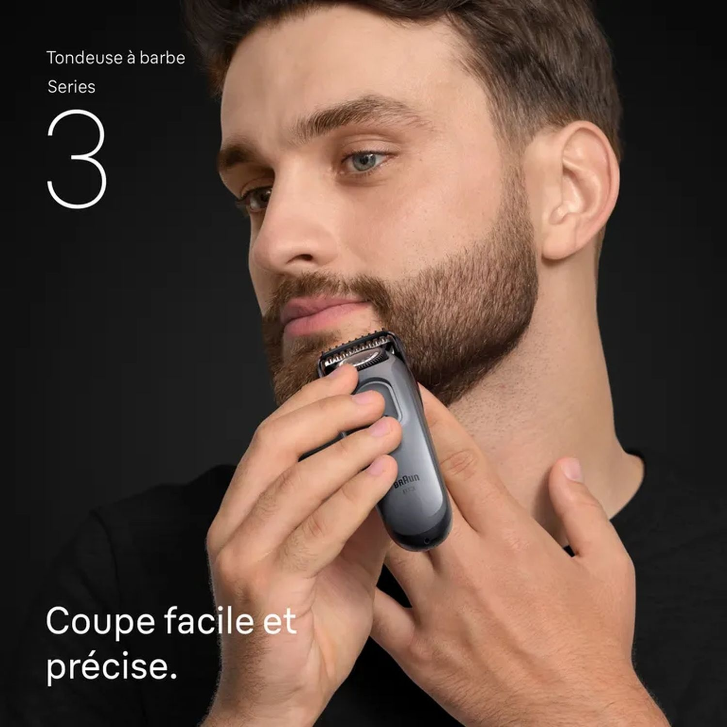 Un homme utilise une tondeuse à barbe noire et grise pour tailler sa barbe, en gros plan.