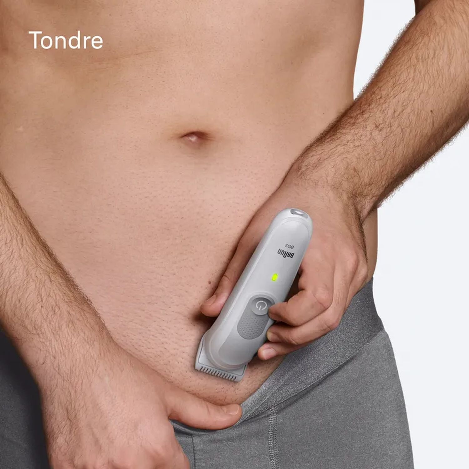 Torse d'une personne avec une tondeuse utilisée sur les poils pubiens. La tondeuse est blanche et grise.