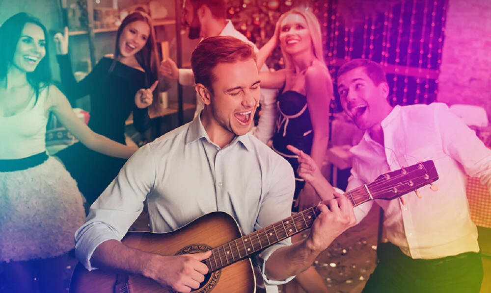 Grupa ludzi tańczących i śpiewających na imprezie, mężczyzna grający na gitarze.