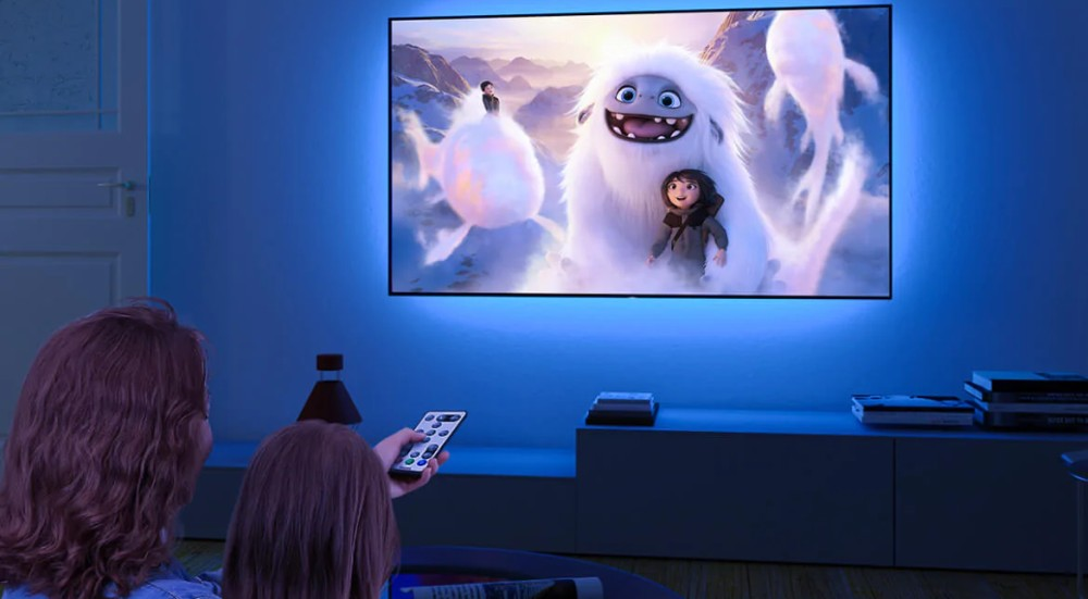 Telewizor wyświetlający film animowany, dwie osoby oglądają, niebieska ściana.