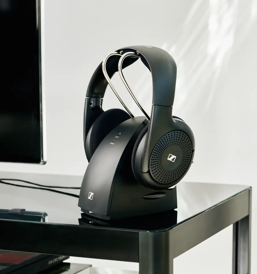 Casque noir sur socle de chargement sur une table, près d'un écran de télévision.