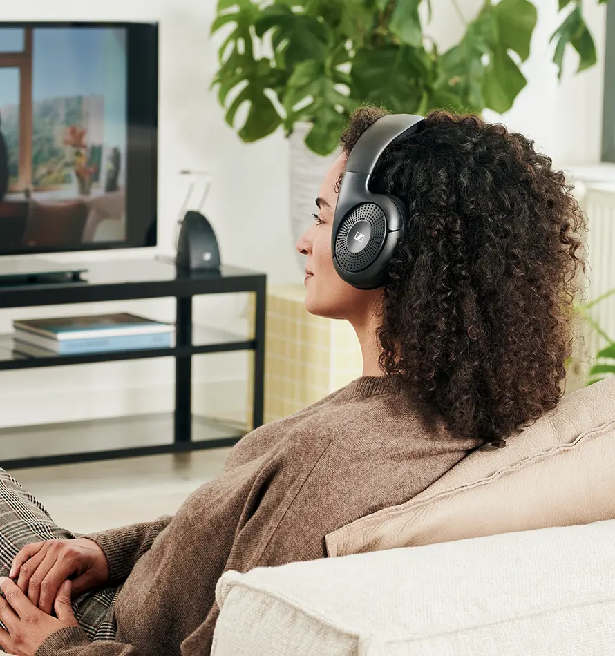 Femme portant un casque, regardant la télévision, avec une plante en arrière-plan.