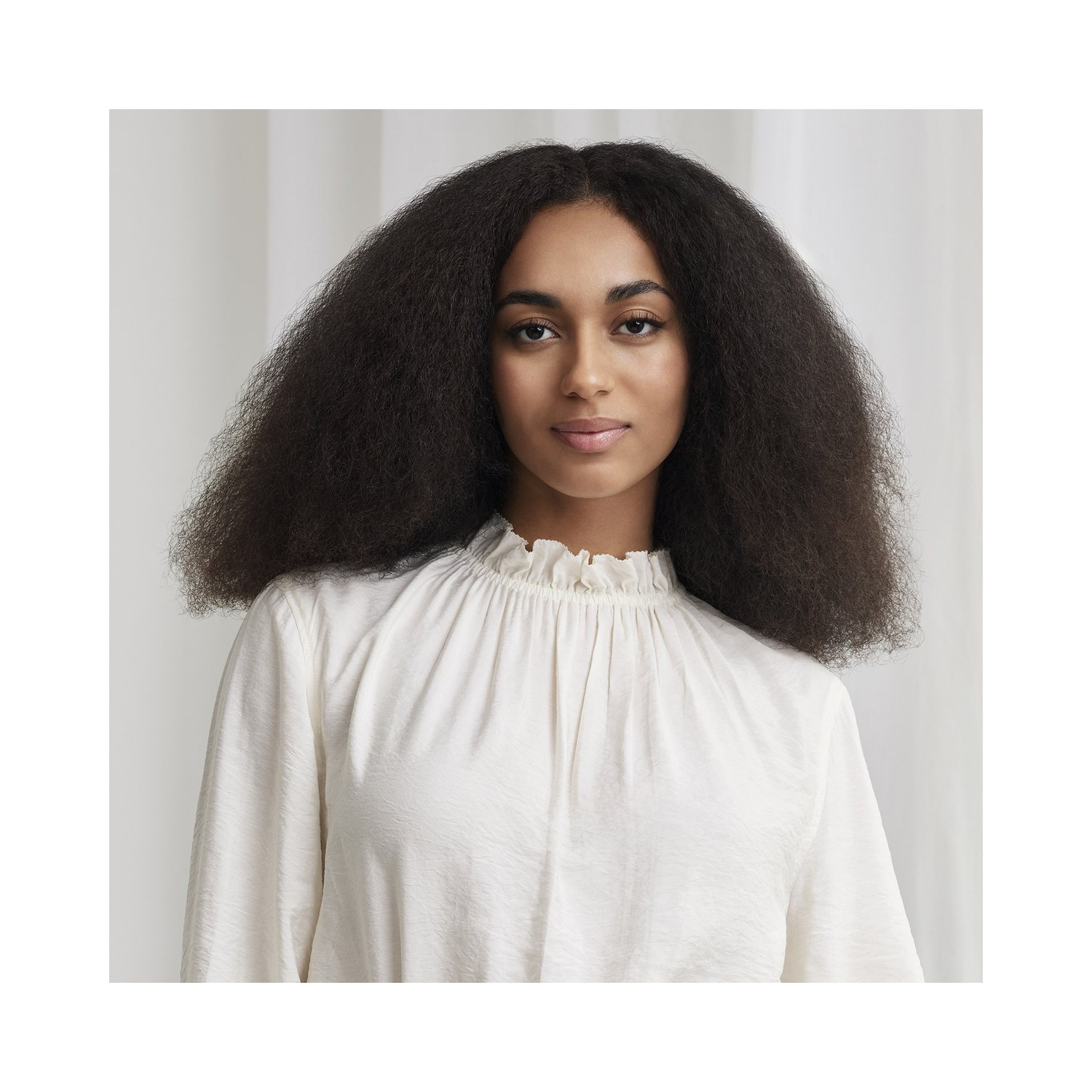 Portret van een vrouw met lang, donker, krullend haar en een witte blouse.