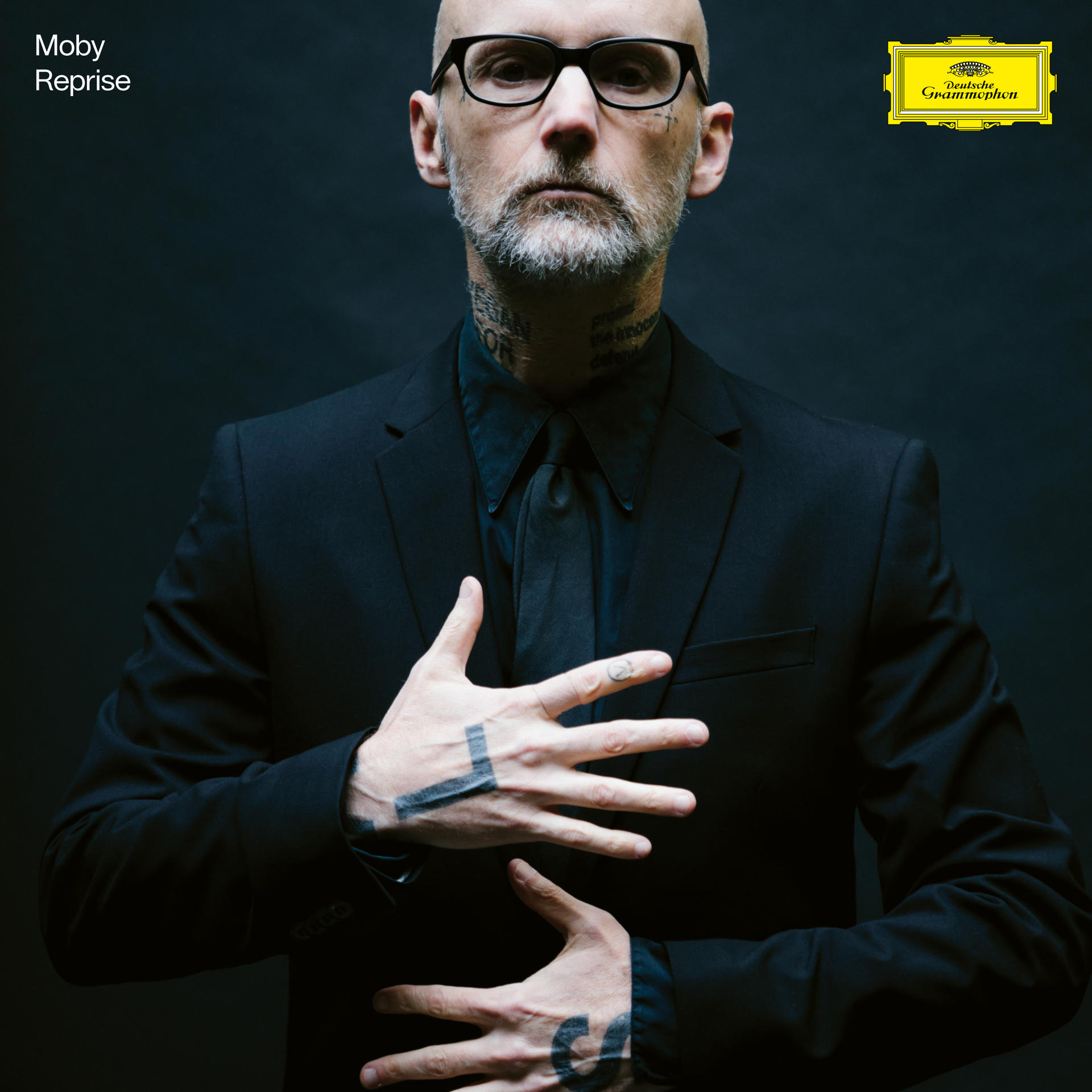 Glatzköpfiger Mann im schwarzen Anzug, Tattoos an Hals und Hand. Schwarzer Hintergrund. Logo Deutsche Grammophon.