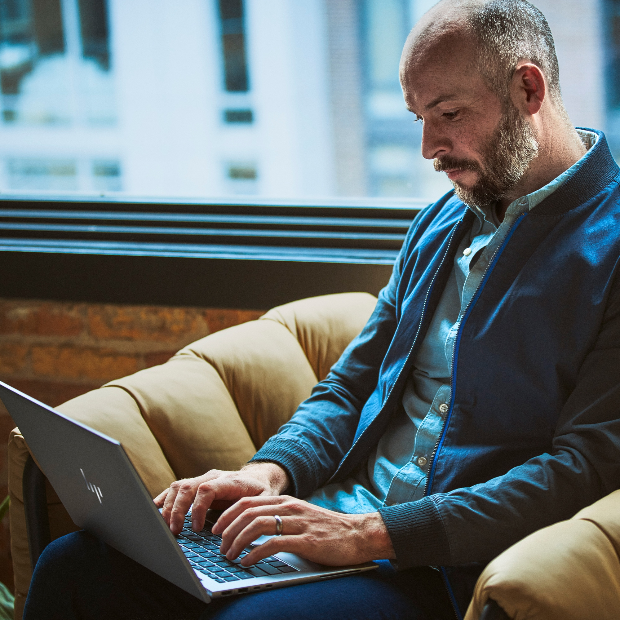 Ein Mann sitzt und arbeitet an einem Laptop, mit einem Fenster im Hintergrund.