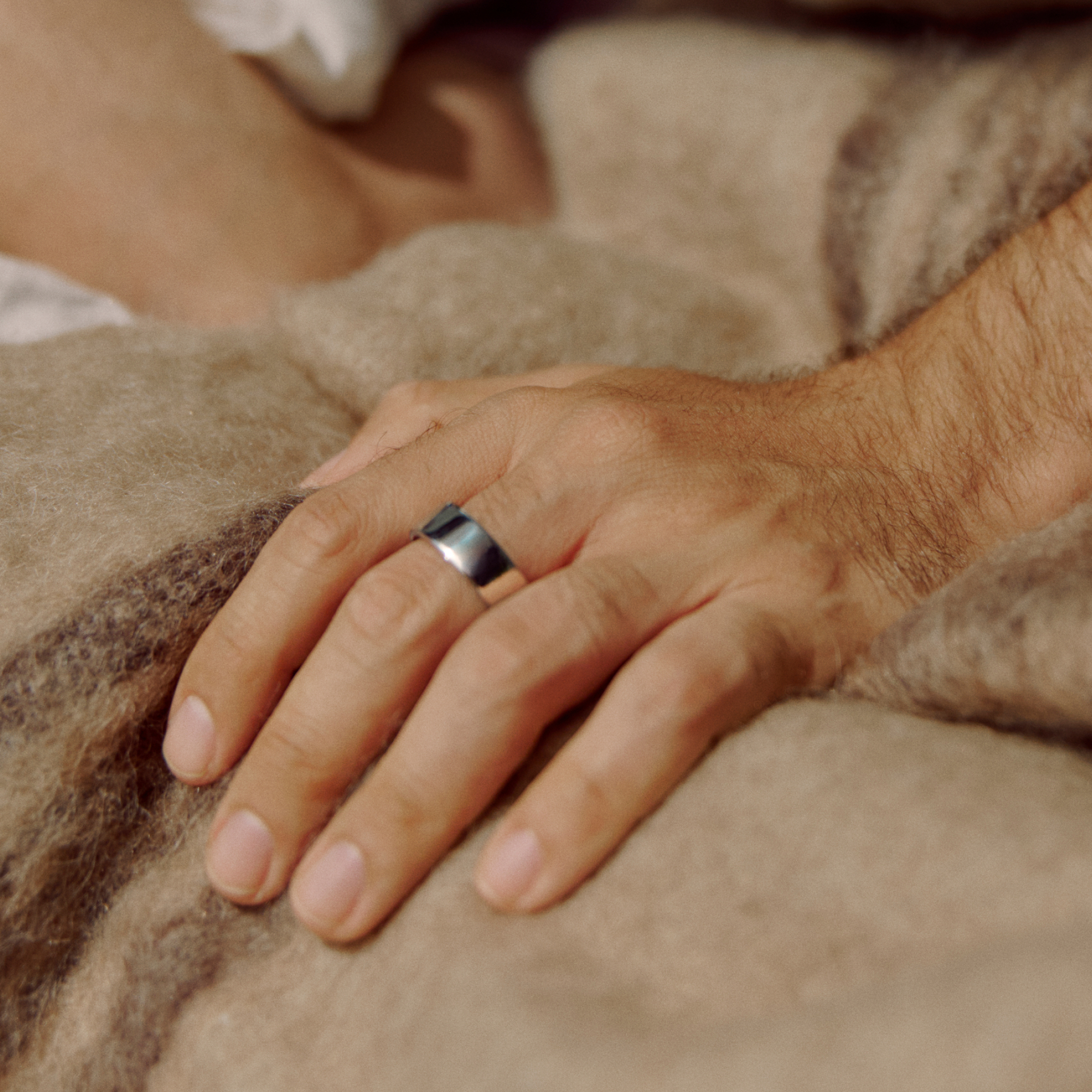 Eine Hand mit einem silbernen Ring, die auf einer braunen Decke ruht.