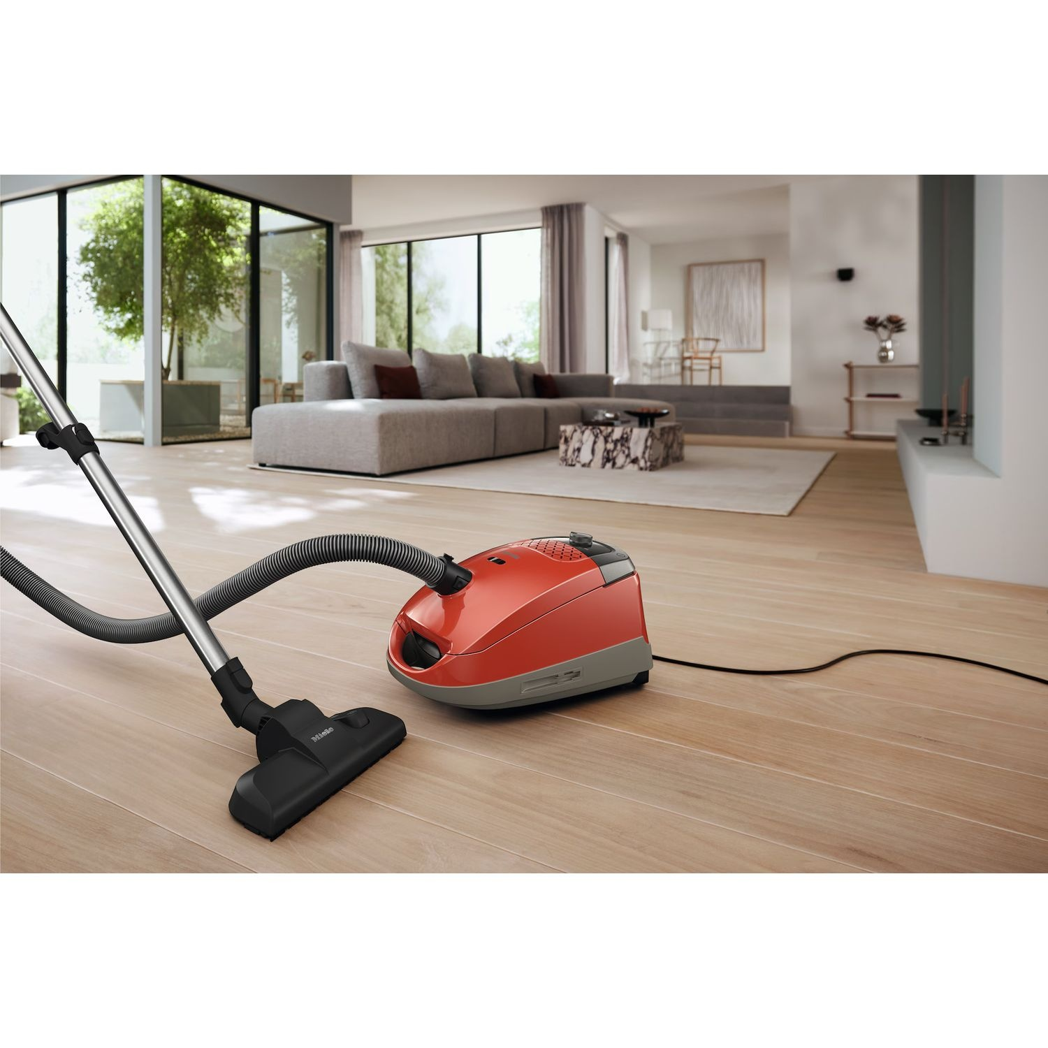 Un aspirateur orange dans une pièce avec des planchers en bois et un canapé, avec un tuyau d'aspirateur.