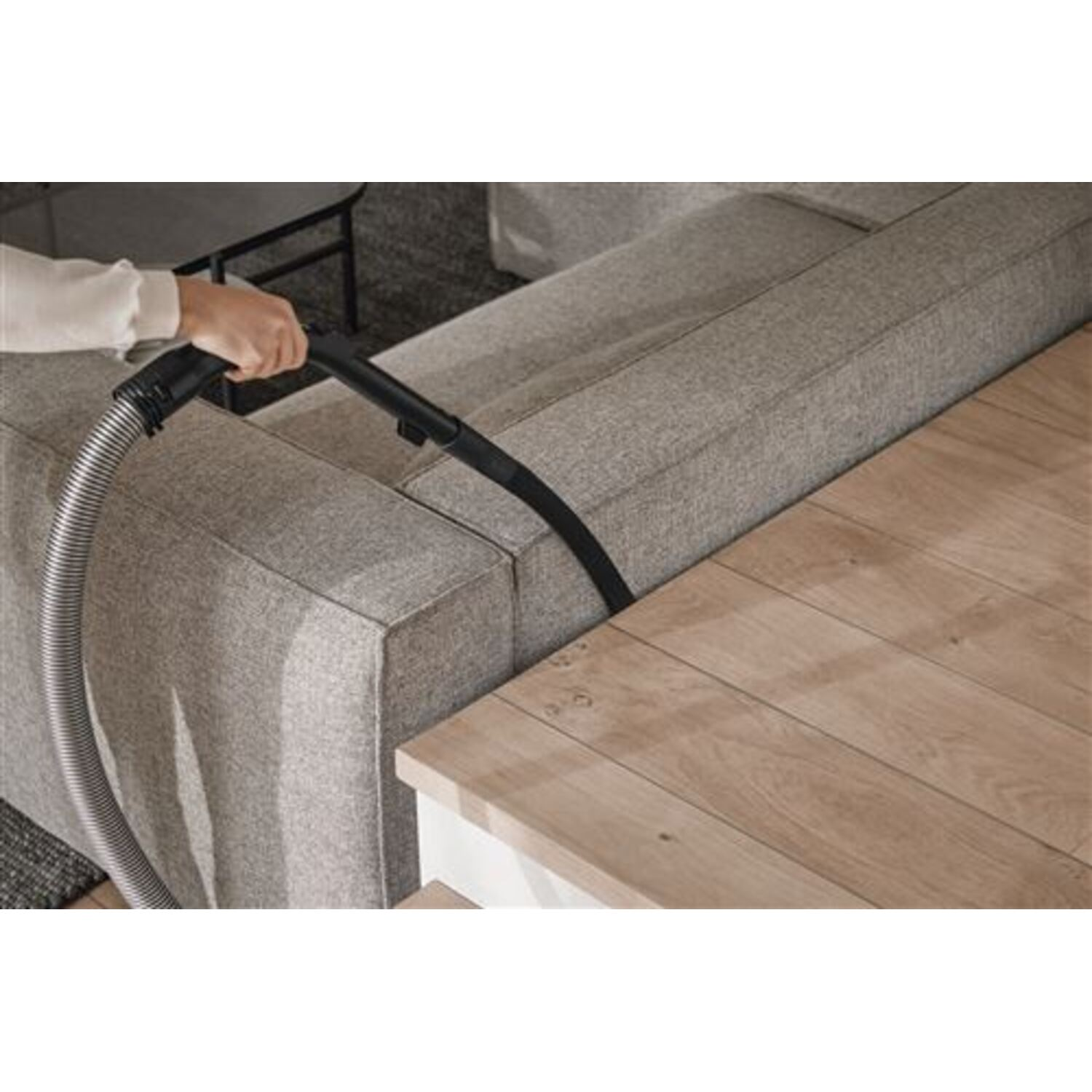 A person vacuuming a sofa with a handheld vacuum cleaner.