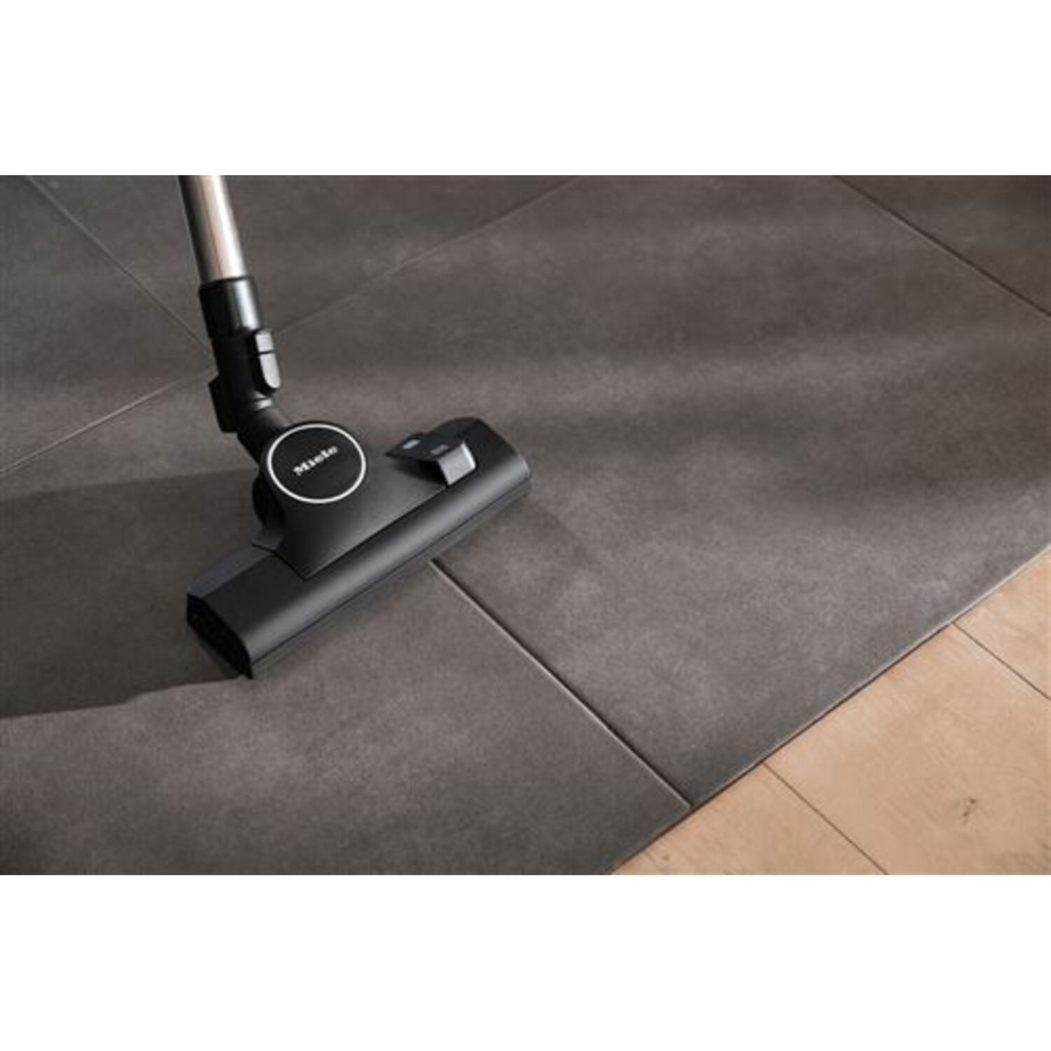 A black vacuum cleaner head on dark gray tiles and wooden floor.