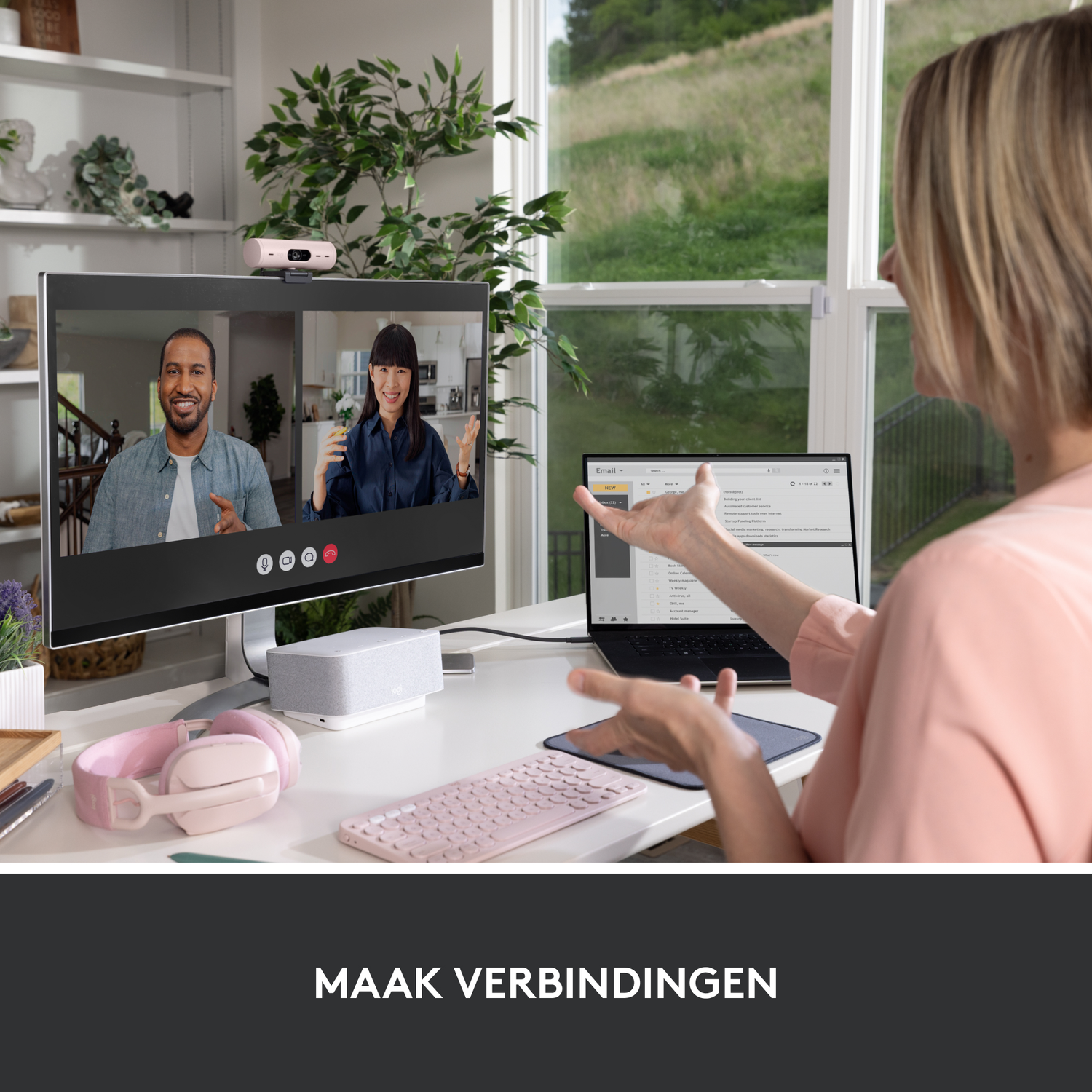 A woman on a video call with two people. A laptop, screen, keyboard, and headphones are visible.