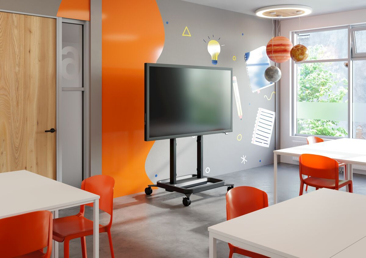 Klassenzimmer mit großem Fernsehbildschirm auf einem Ständer, Tischen, Stühlen und Fenstern.