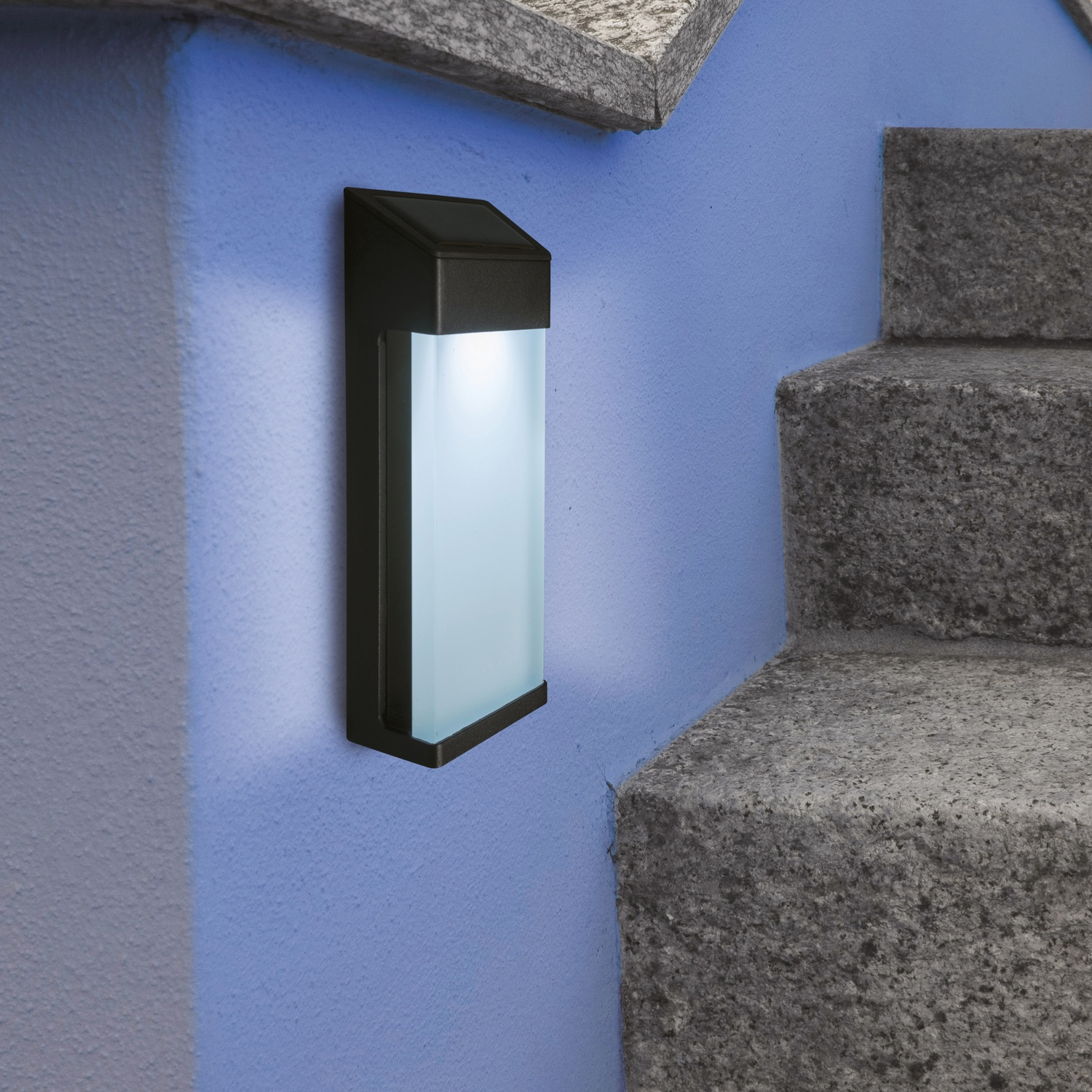 Lampada esterna nera con pannello in vetro smerigliato, montata su muro blu vicino scale.